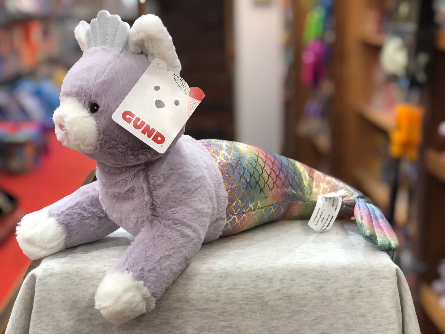 Gund plush cat mermaid with iridescent rainbow tail and shell crown, 18-inch soft toy on display in store