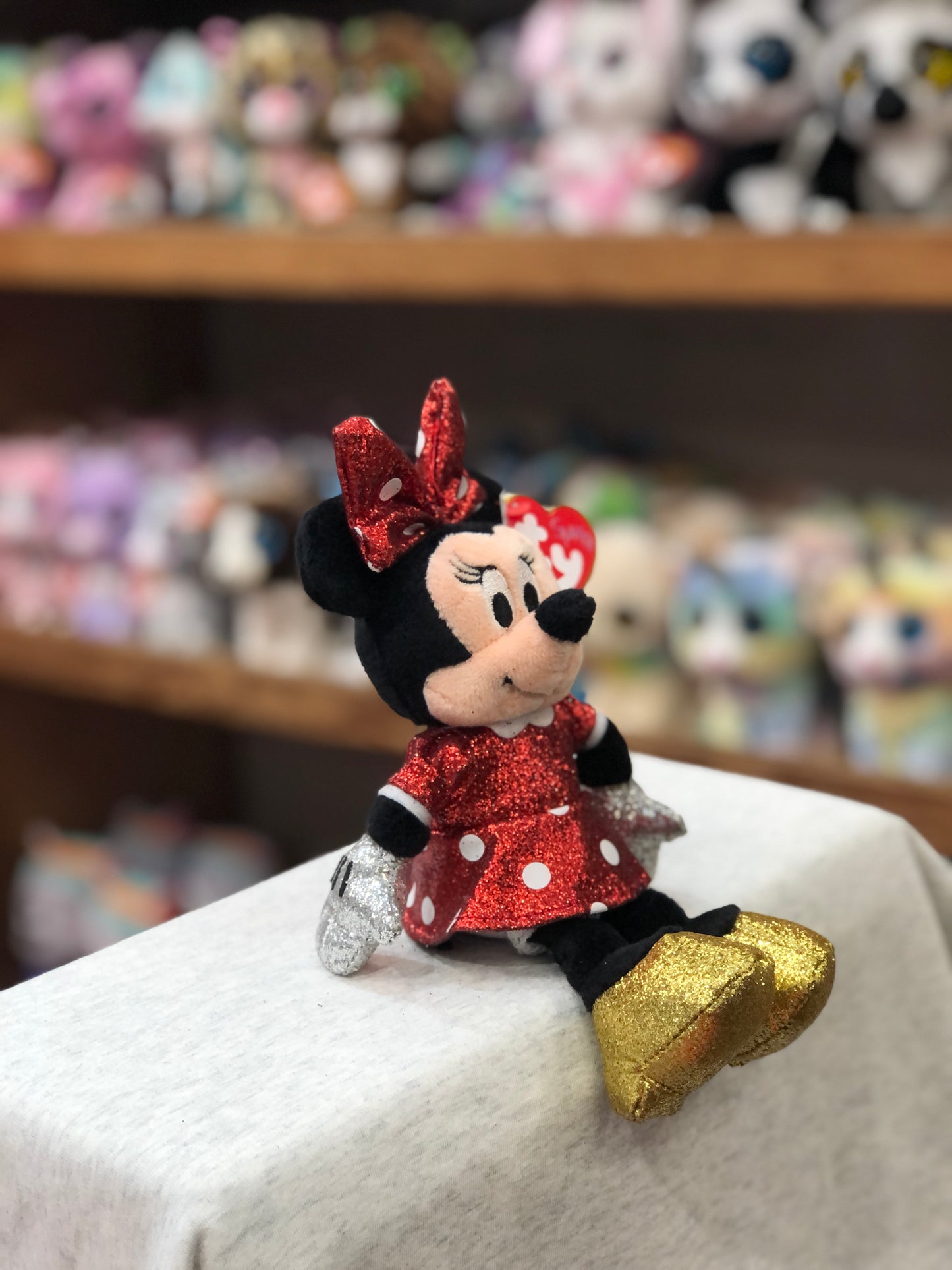 Ty Minnie Mouse red sparkle plush toy sitting on display, with other stuffed animals in background