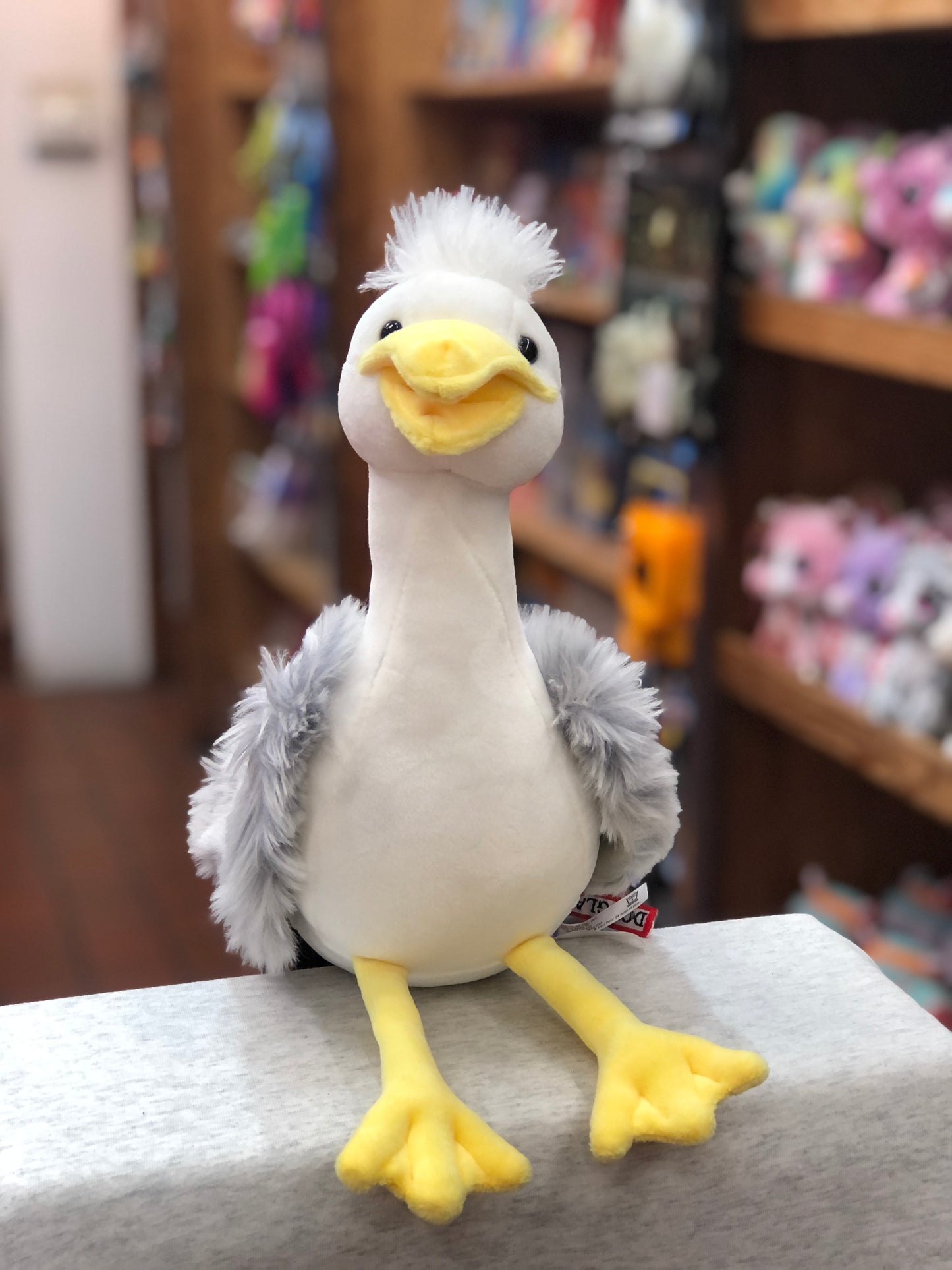 Cute Douglas Macaroon Seagull plush toy with white body, gray wings, yellow beak and feet, sitting on display in toy store