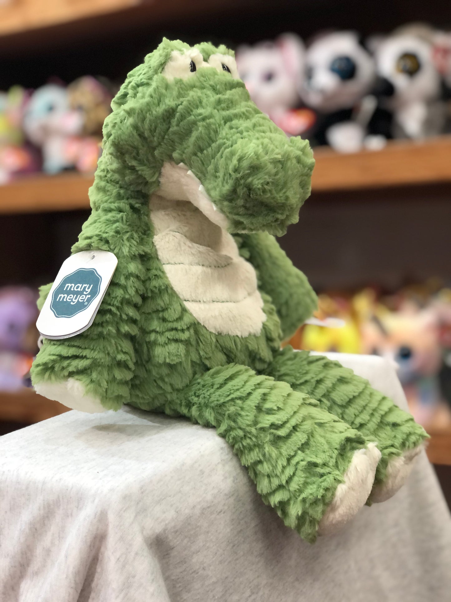 Soft green Mary Meyer Marshmallow Gator plush toy sitting on display, showcasing its cuddly texture and floppy design