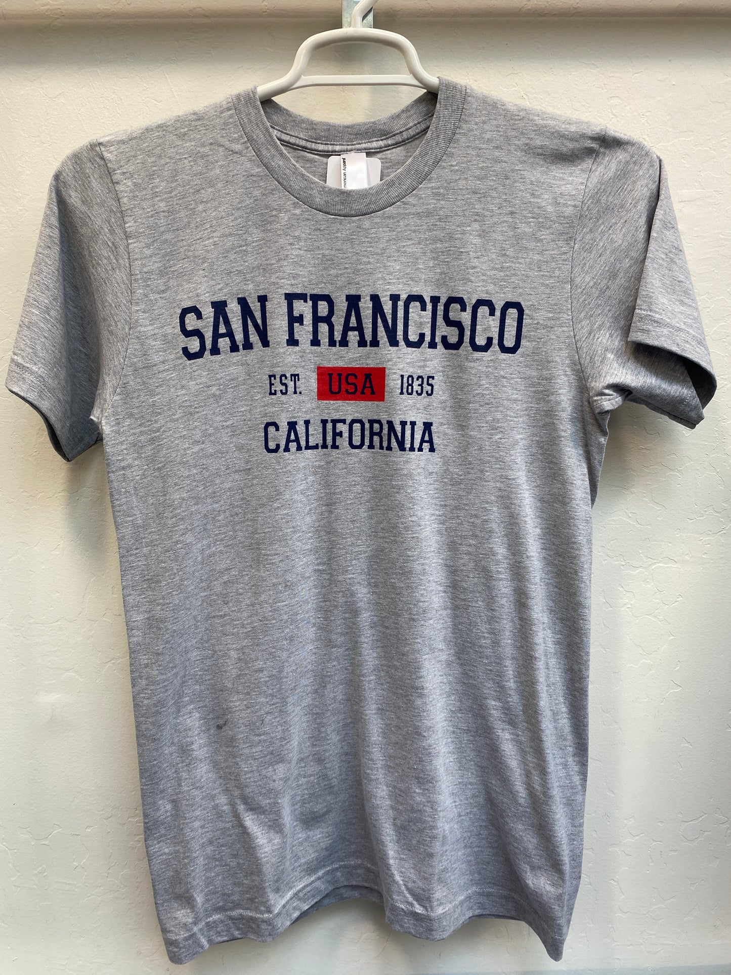 Gray cotton t-shirt with "San Francisco California Est. USA 1835" printed in navy and red, hanging on white hanger