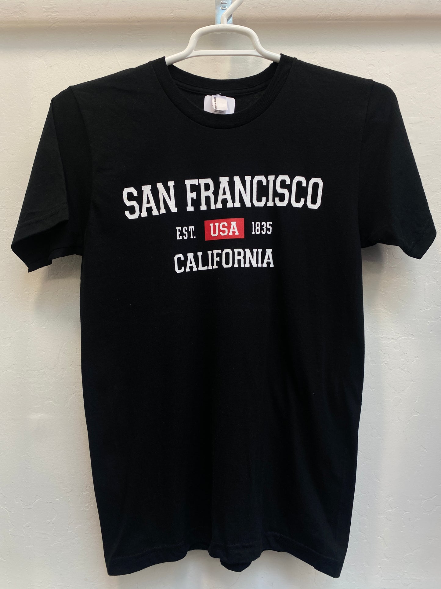 Black cotton t-shirt with "San Francisco California Est. USA 1835" text, hanging on display