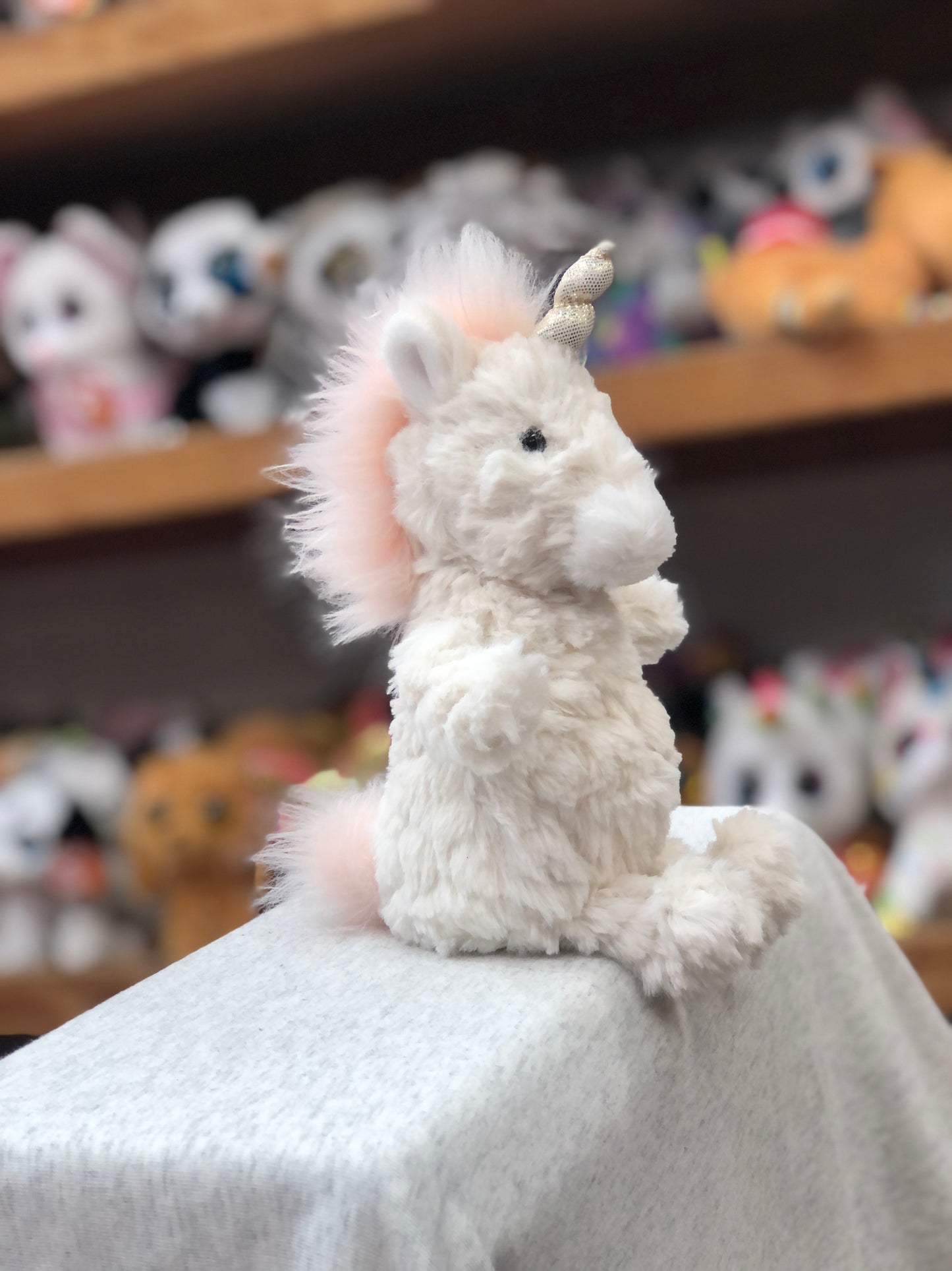 Soft white unicorn Puttling plush toy with pink mane, sitting on display with other stuffed animals in background