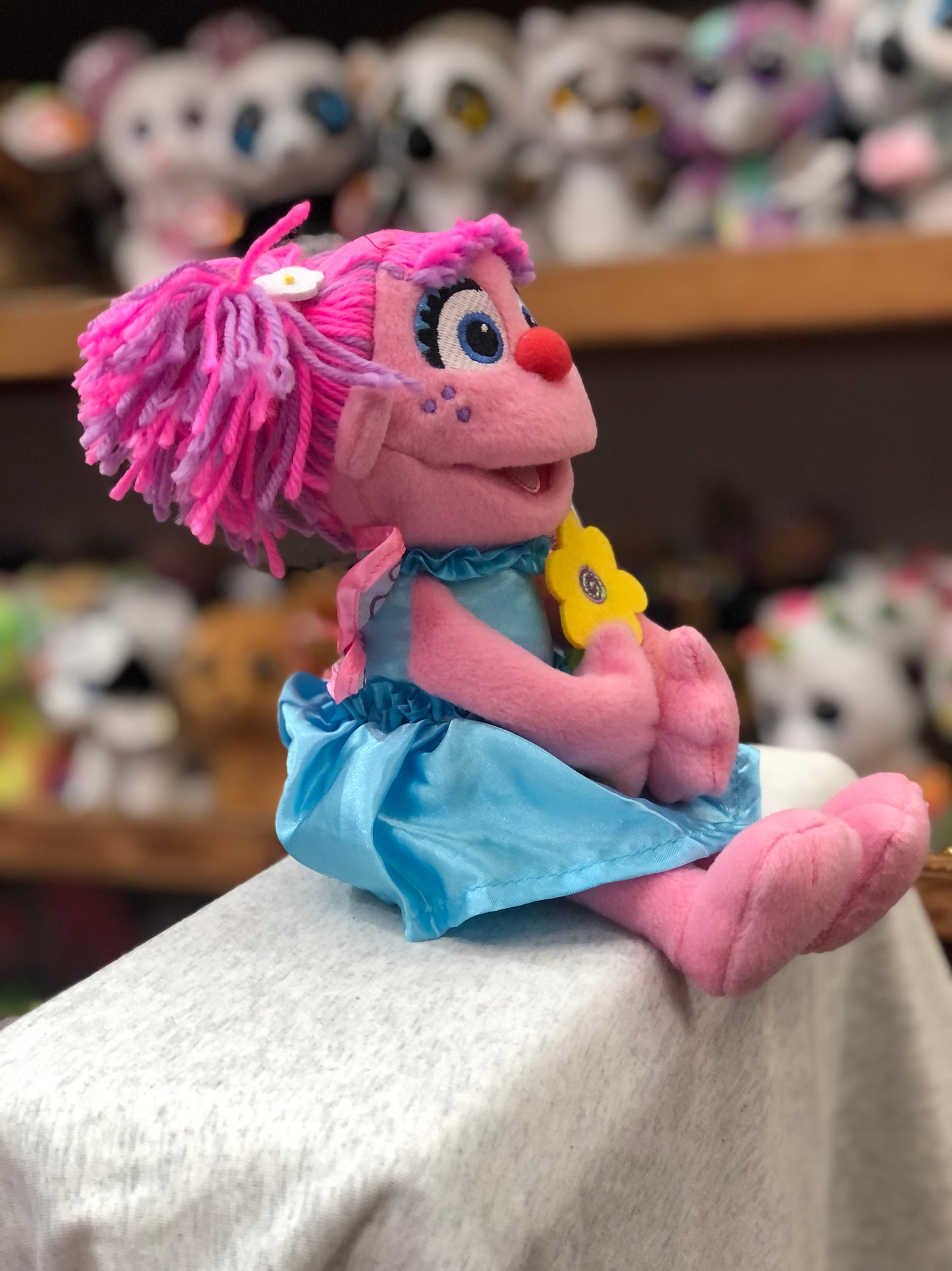 Gund Sesame Street Abby Cadabby plush toy with pink hair and blue dress holding yellow flower, sitting on display