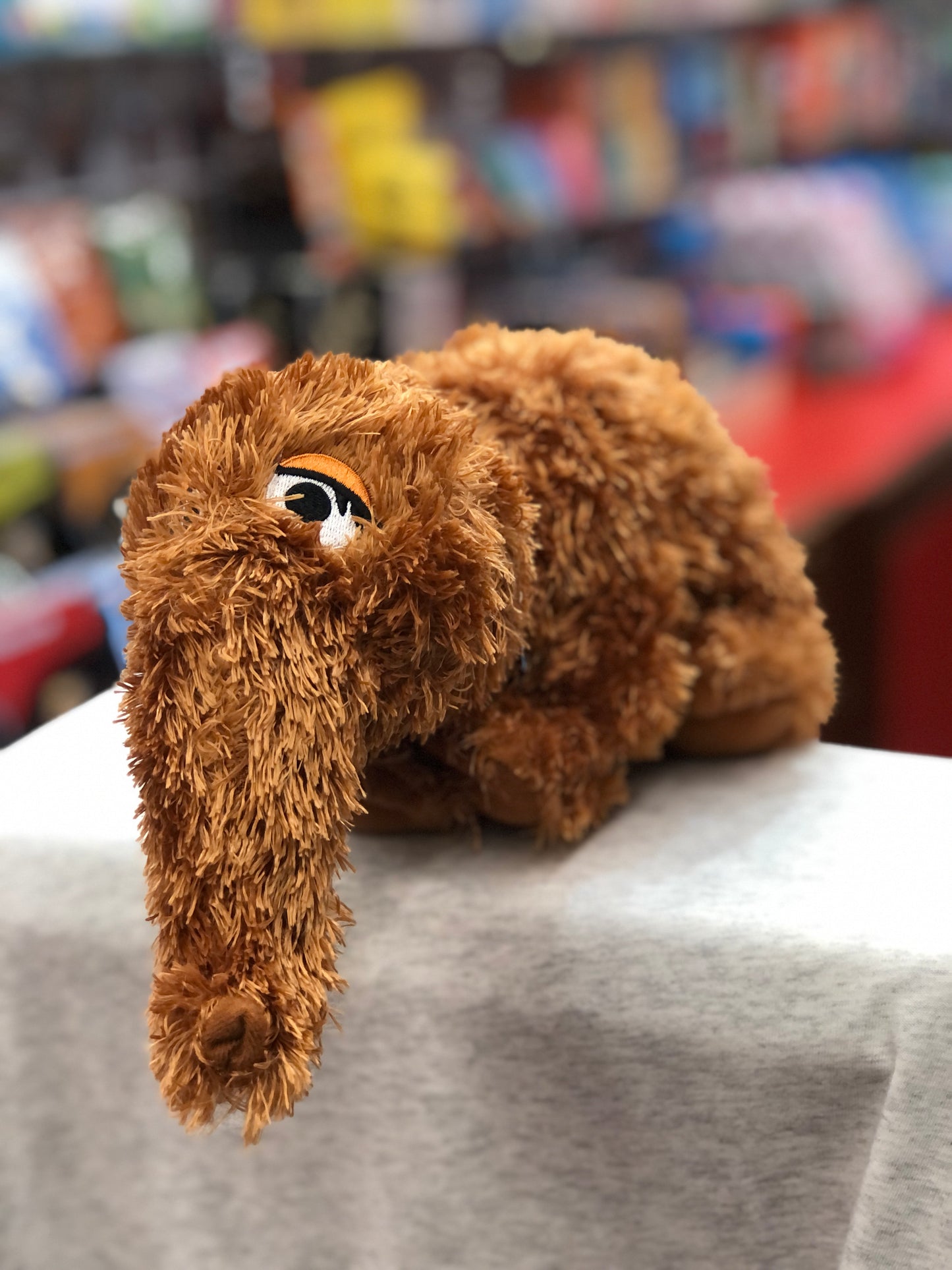 Gund Sesame Street Snuffleupagus plush toy, brown and furry, displayed on shelf with colorful background
