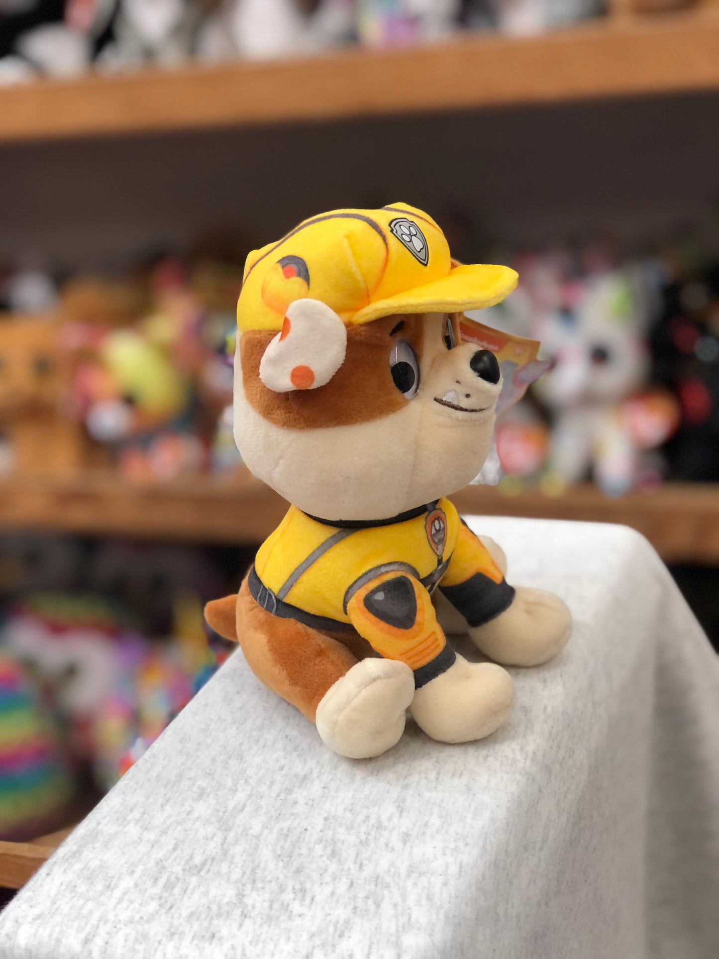 Gund Paw Patrol: The Movie Rubble plush toy in yellow construction uniform, sitting on display with colorful background