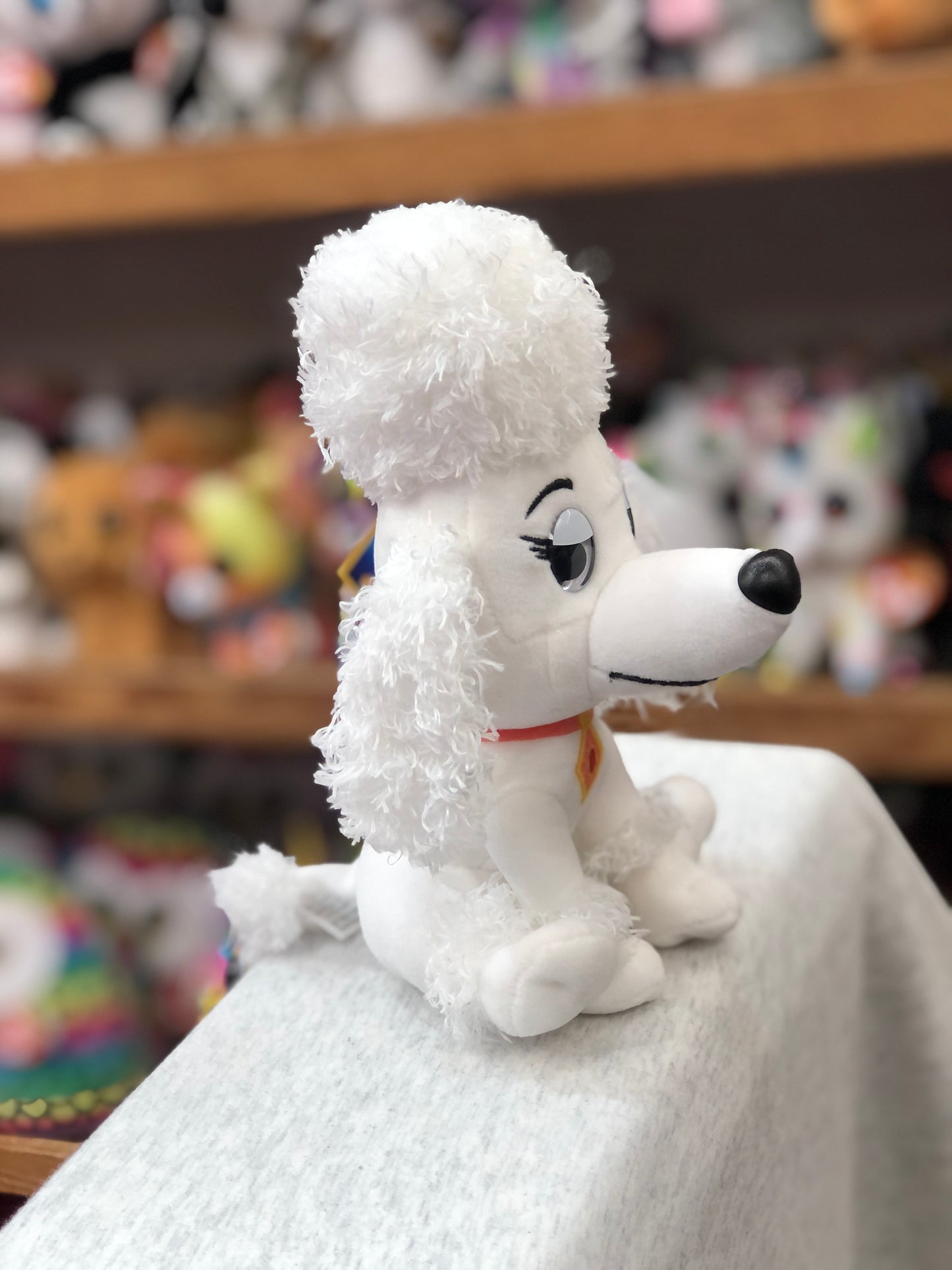 Gund Paw Patrol Delores plush toy, white poodle with fluffy hair, embroidered eyes, and red collar, sitting on display