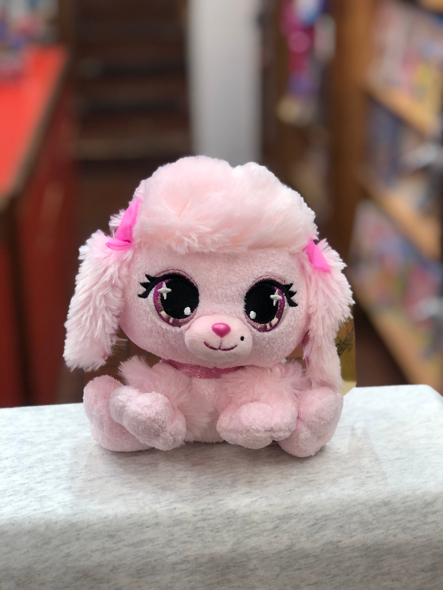 Gund P.Lushes Pinkie Monroe poodle plush toy with sparkly eyes, pink fur, and glitter collar, sitting on display