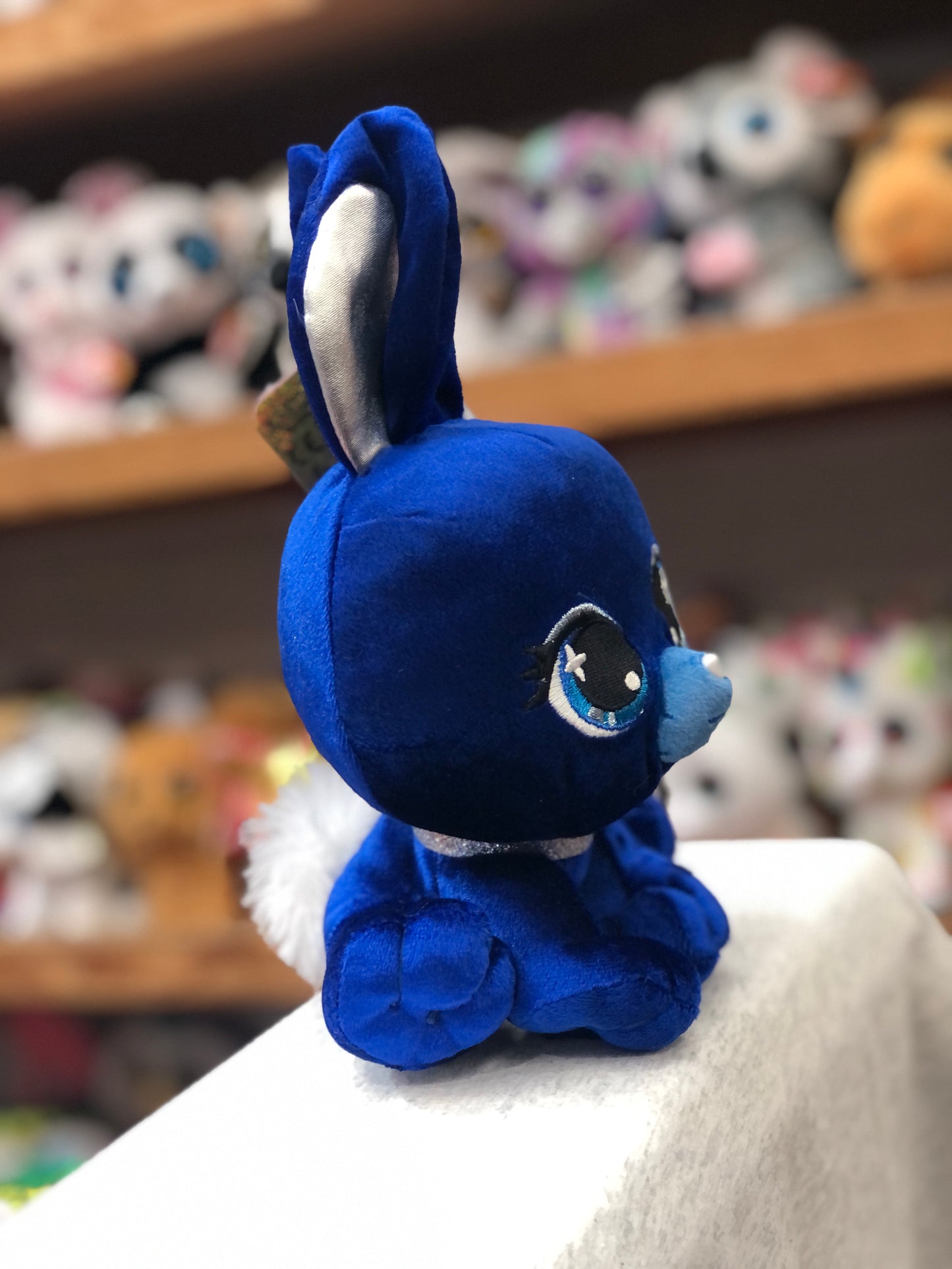 Gund P.Lushes Zuri Karrats plush bunny in deep blue velvet with silver ears and glittery eyeshadow, sitting on display shelf