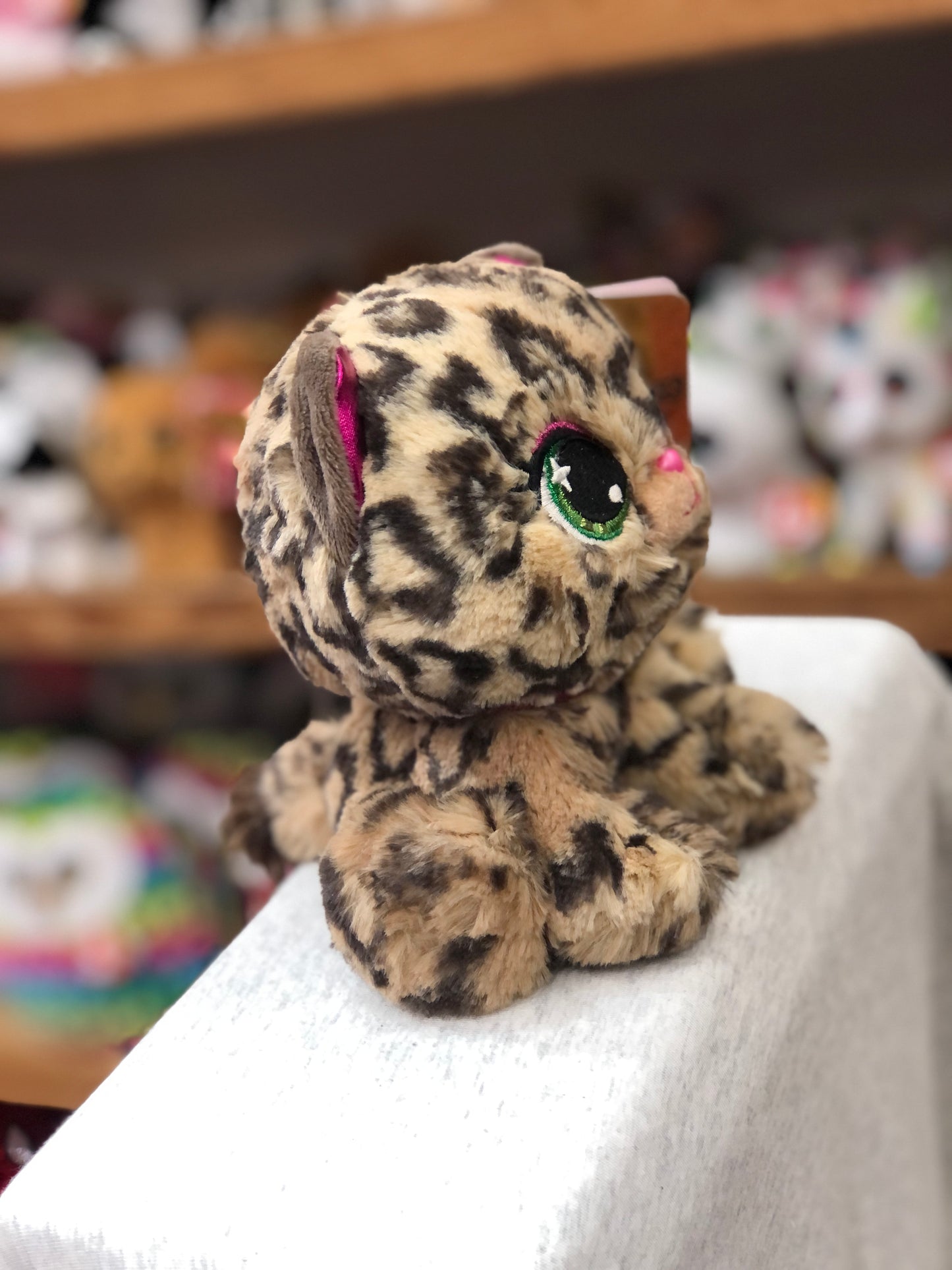 Gund P.Lushes Sadie Spotson plush leopard toy with pink ears and green eyes, sitting on display in a toy store
