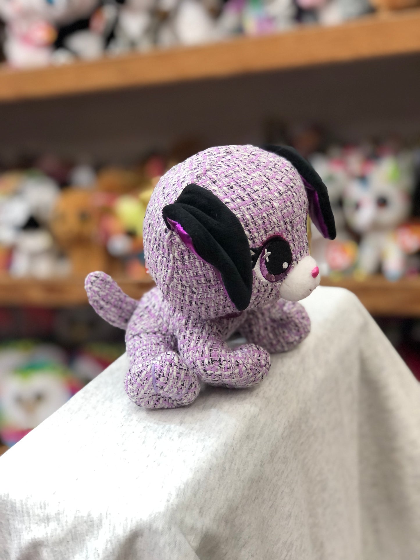 Gund P.Lushes Michelle Boucle plush toy, purple tweed texture, black ears, pink accents, displayed on shelf with other toys