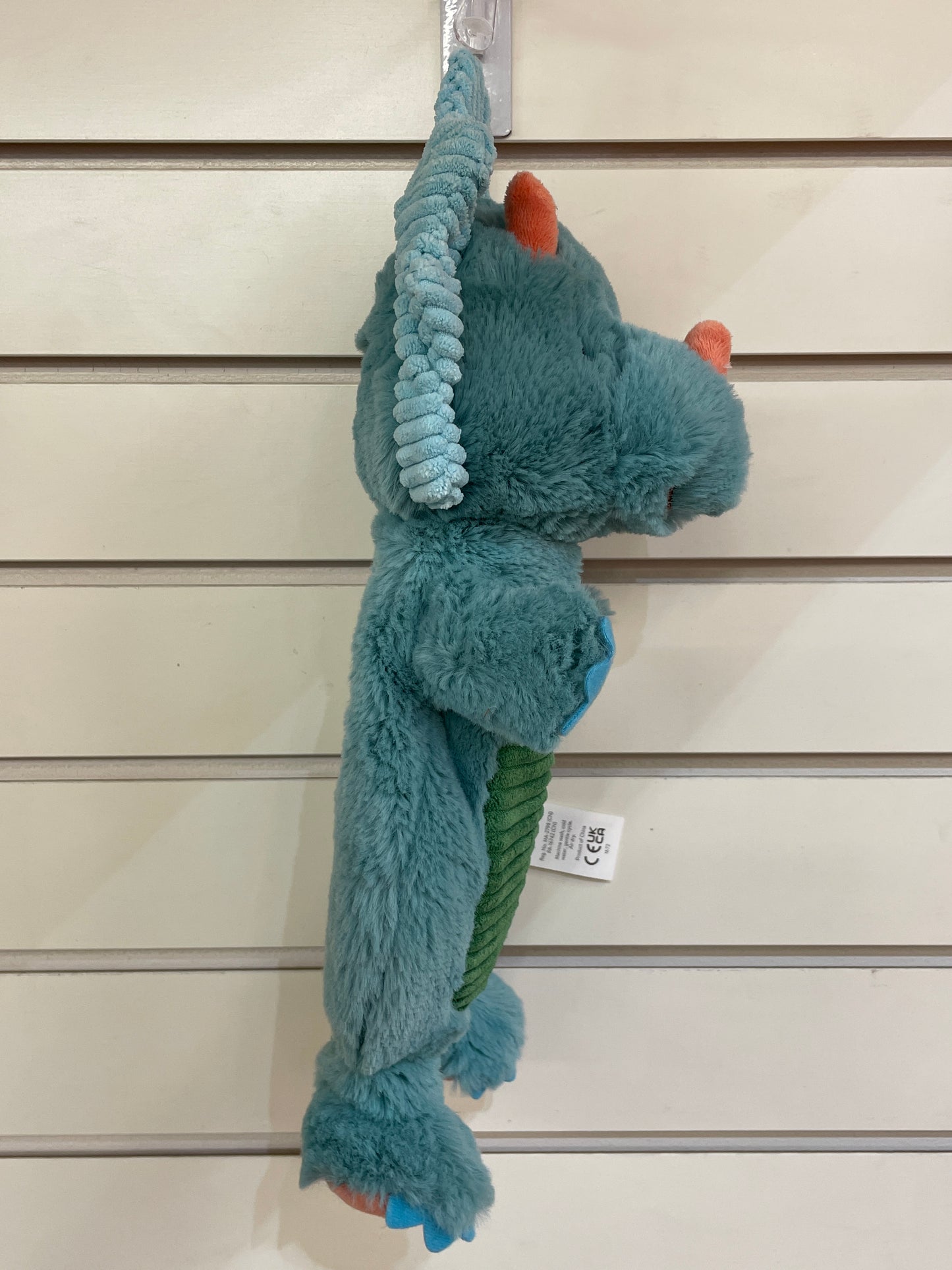 Soft teal dinosaur baby lovey with colorful accents, hanging on display. Plush Pebblesaurus toy for infants, 13 inches long.