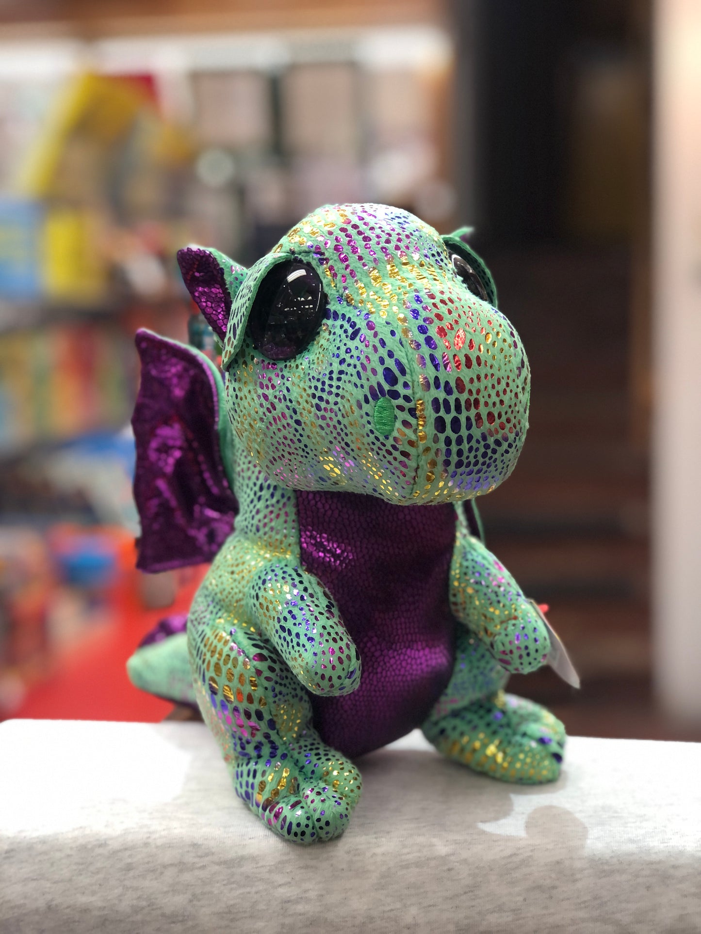 Ty Beanie Boo Cinder dragon plush toy with sparkly green scales, purple wings, and large eyes, sitting on display shelf