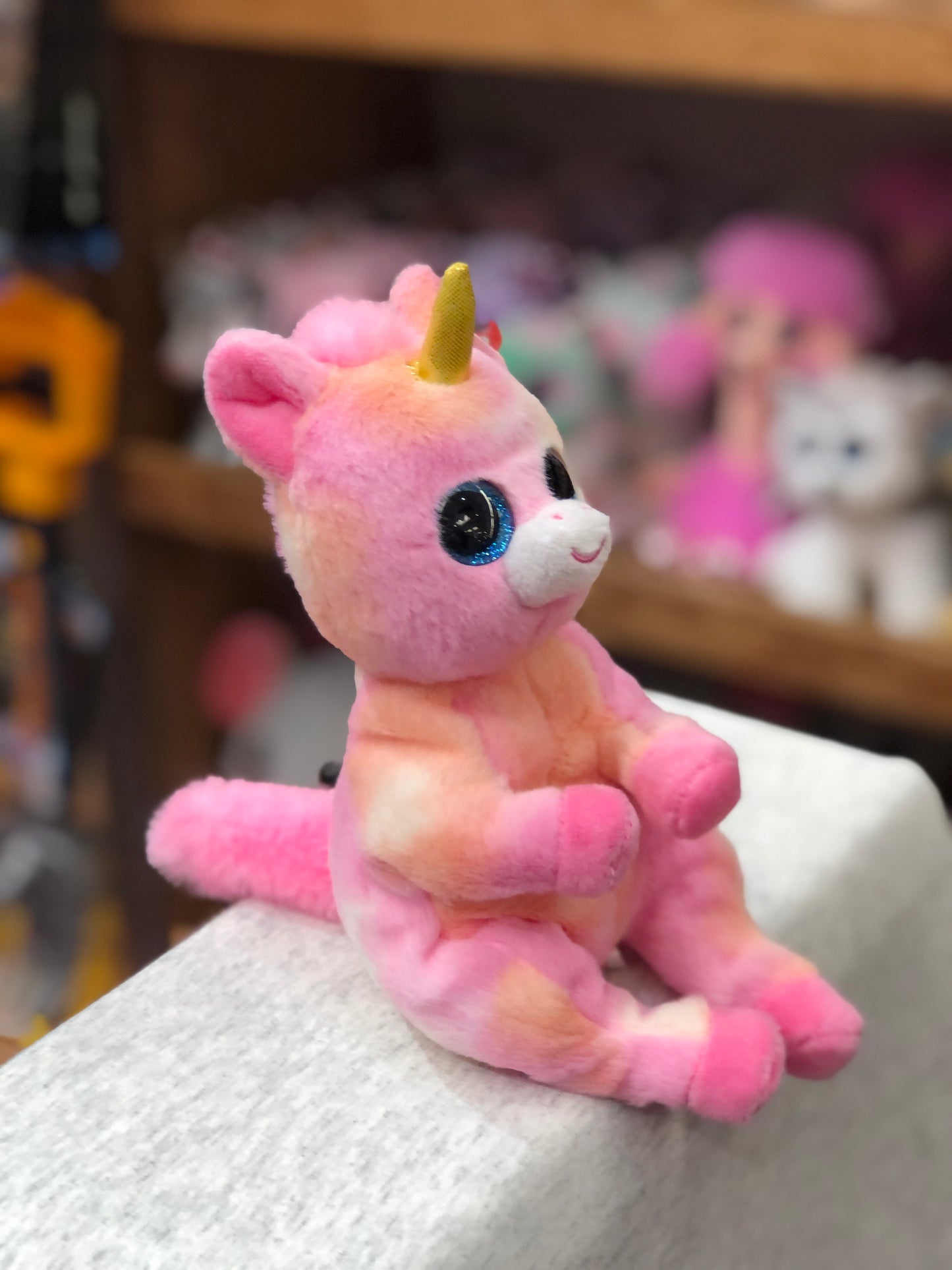 Cute pink Ty Beanie Belly unicorn plush toy with sparkly blue eyes and gold horn, sitting on display shelf