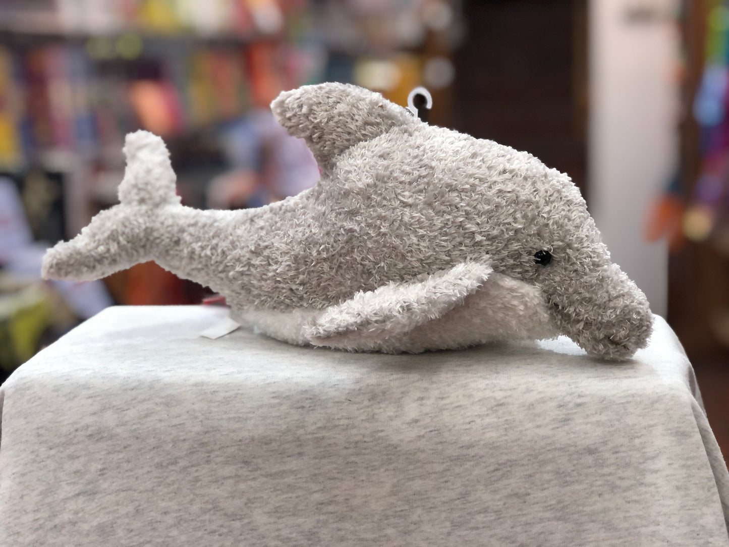Soft gray dolphin plush toy with realistic markings and shiny eyes, displayed on a light surface in a colorful store setting