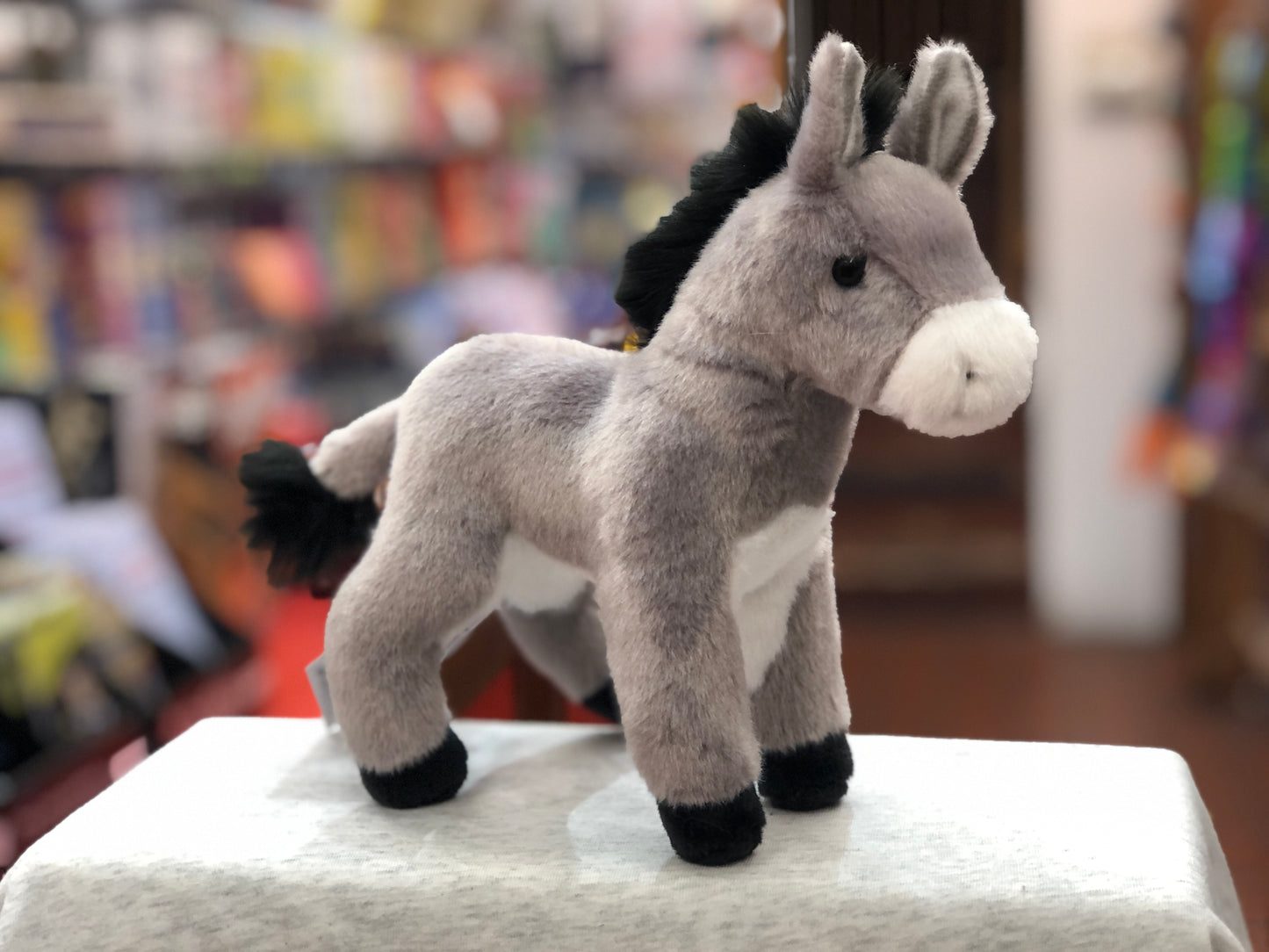 Soft, cuddly Douglas Bordon Burro plush toy with realistic grey and white fur, standing on display in a toy store