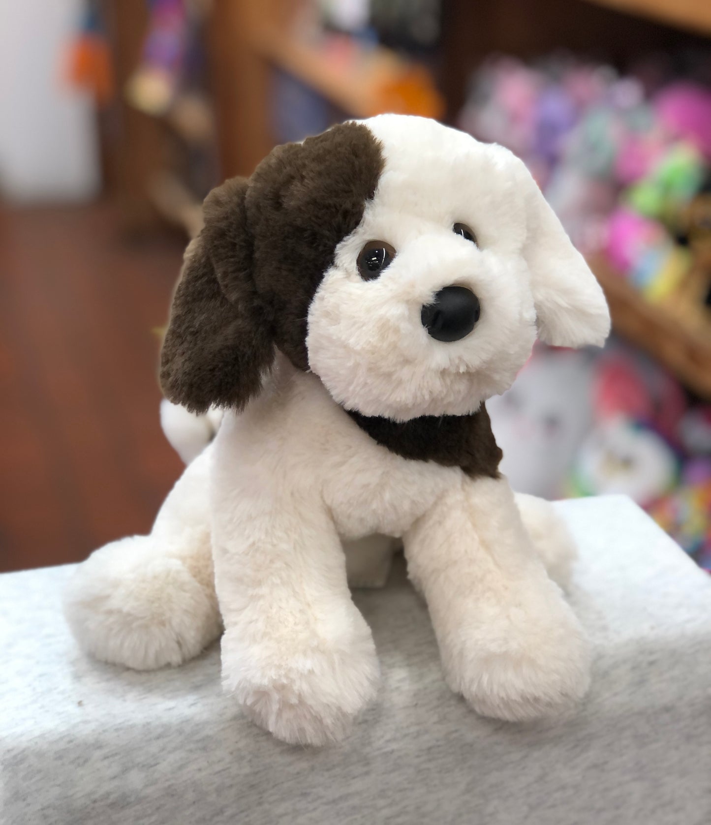 Adorable Douglas Donnie soft puppy plush toy with floppy ears, white and brown fur, sitting on display in a toy store
