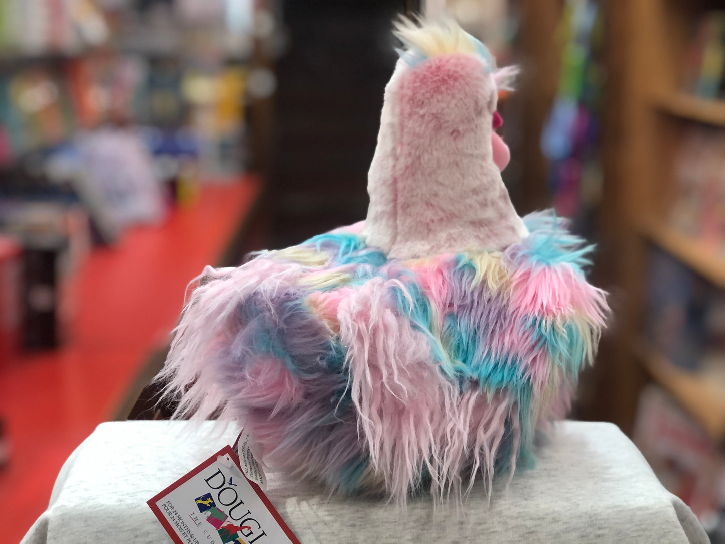 Colorful pastel hen plush toy with fluffy pink, purple, and teal feathers, showcasing Douglas brand tag in store display