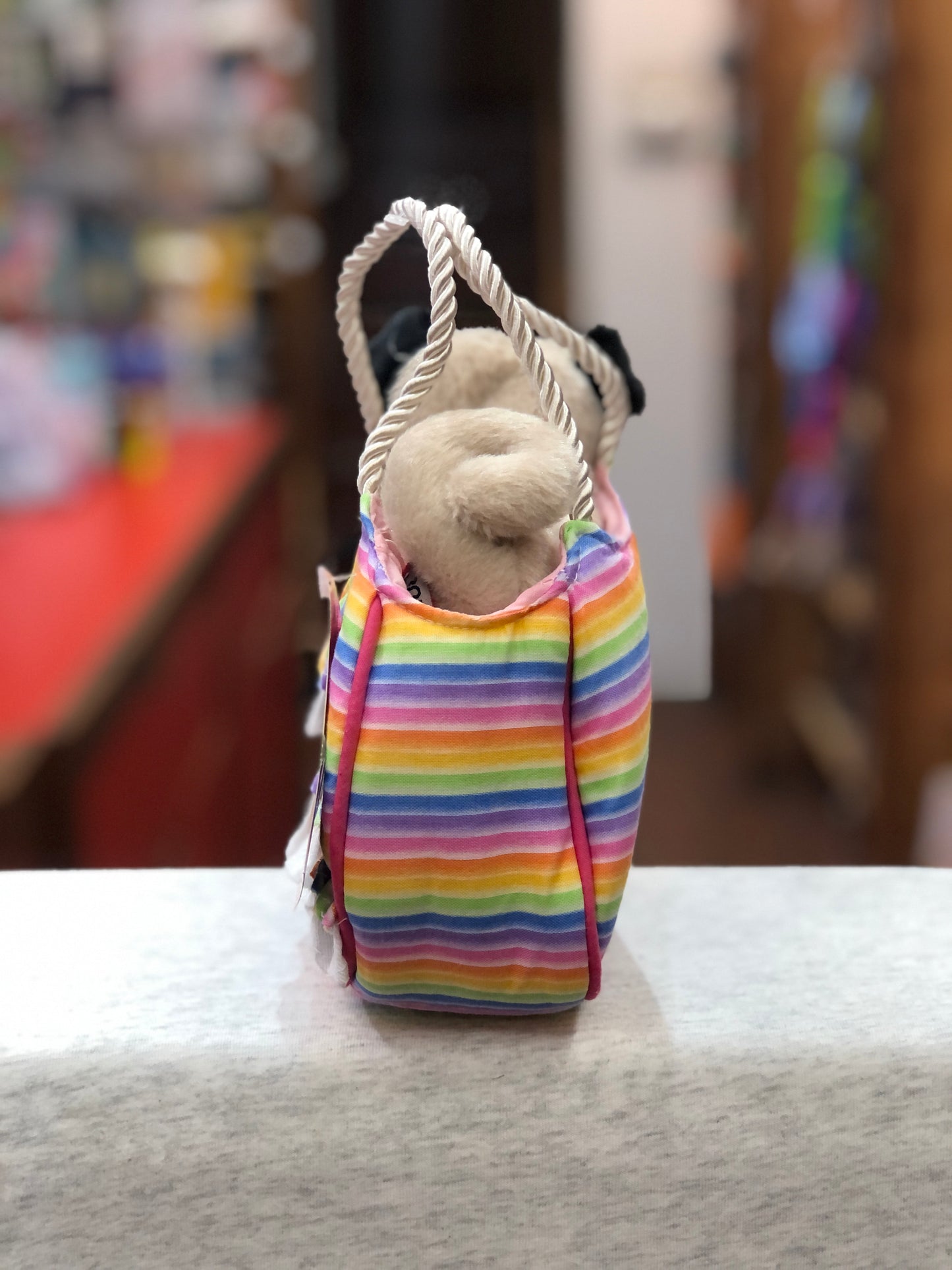 Rainbow-striped children's purse with pug stuffed animal peeking out, featuring ruffles and rope handles