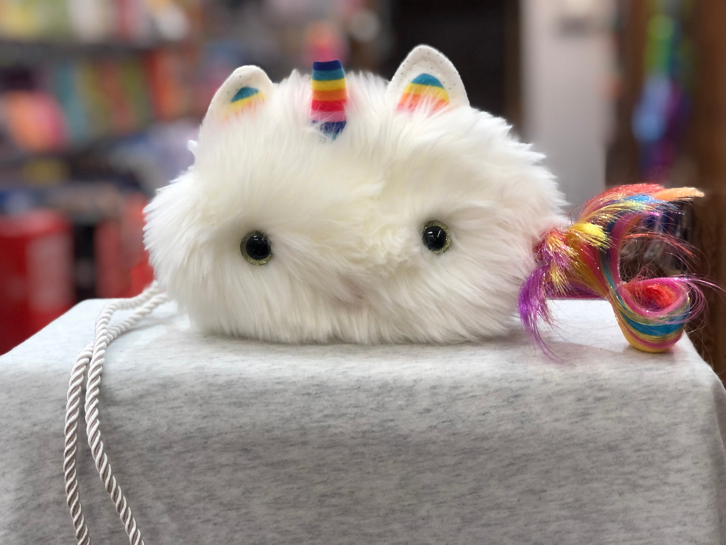 Fluffy white Caticorn crossbody purse with rainbow horn and tail, featuring cute cat ears and green eyes