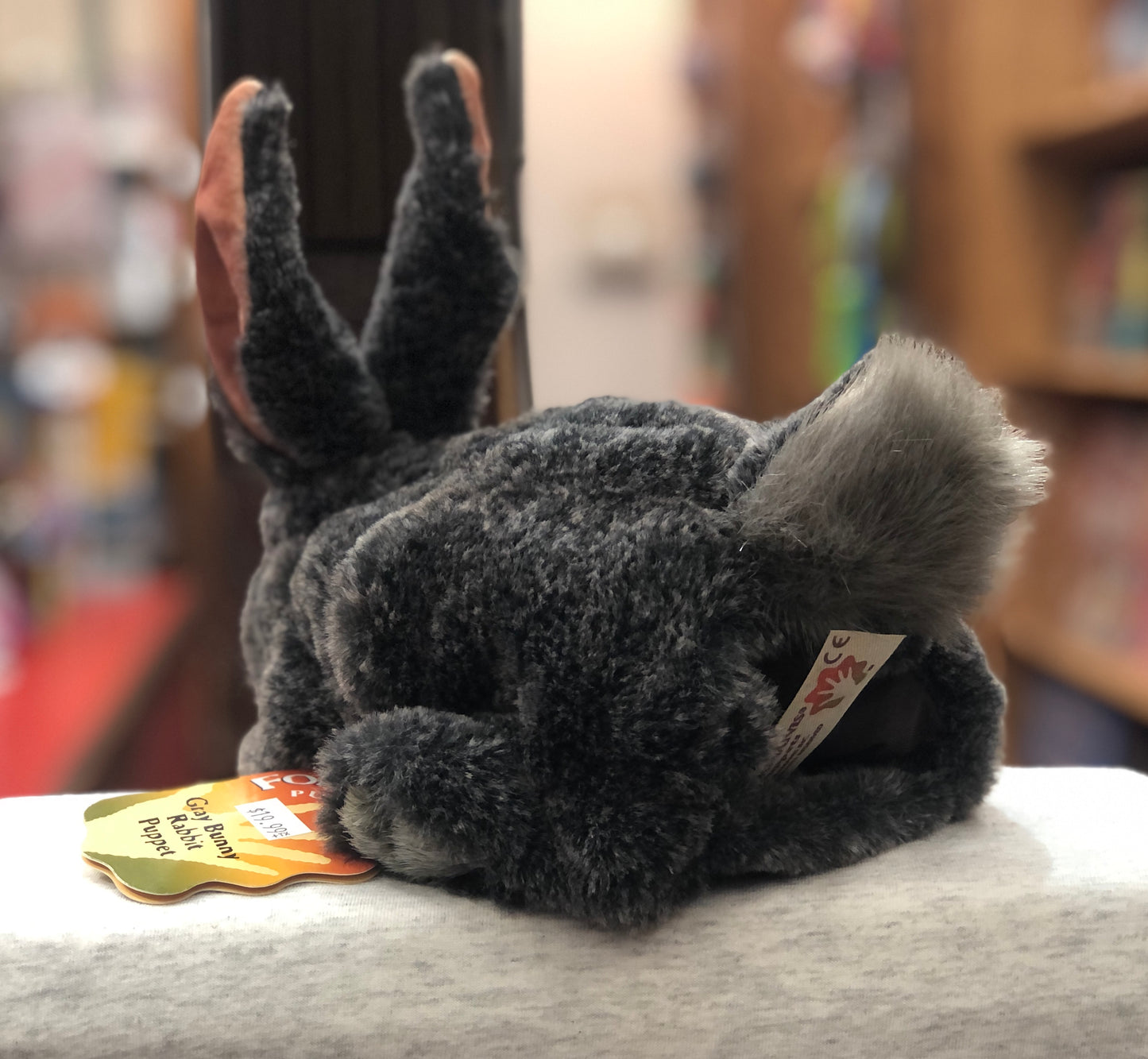 Folkmanis 9" Gray Bunny Rabbit puppet with soft fur, movable ears and legs, shown with product tag in a store setting