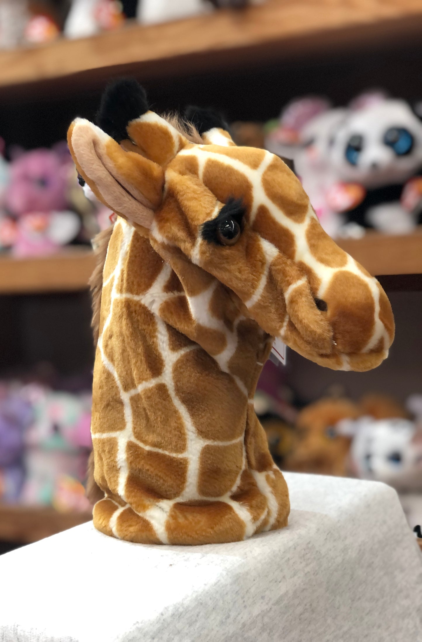 Plush giraffe hand puppet from CarPets collection, displayed on shelf with other animal toys in background