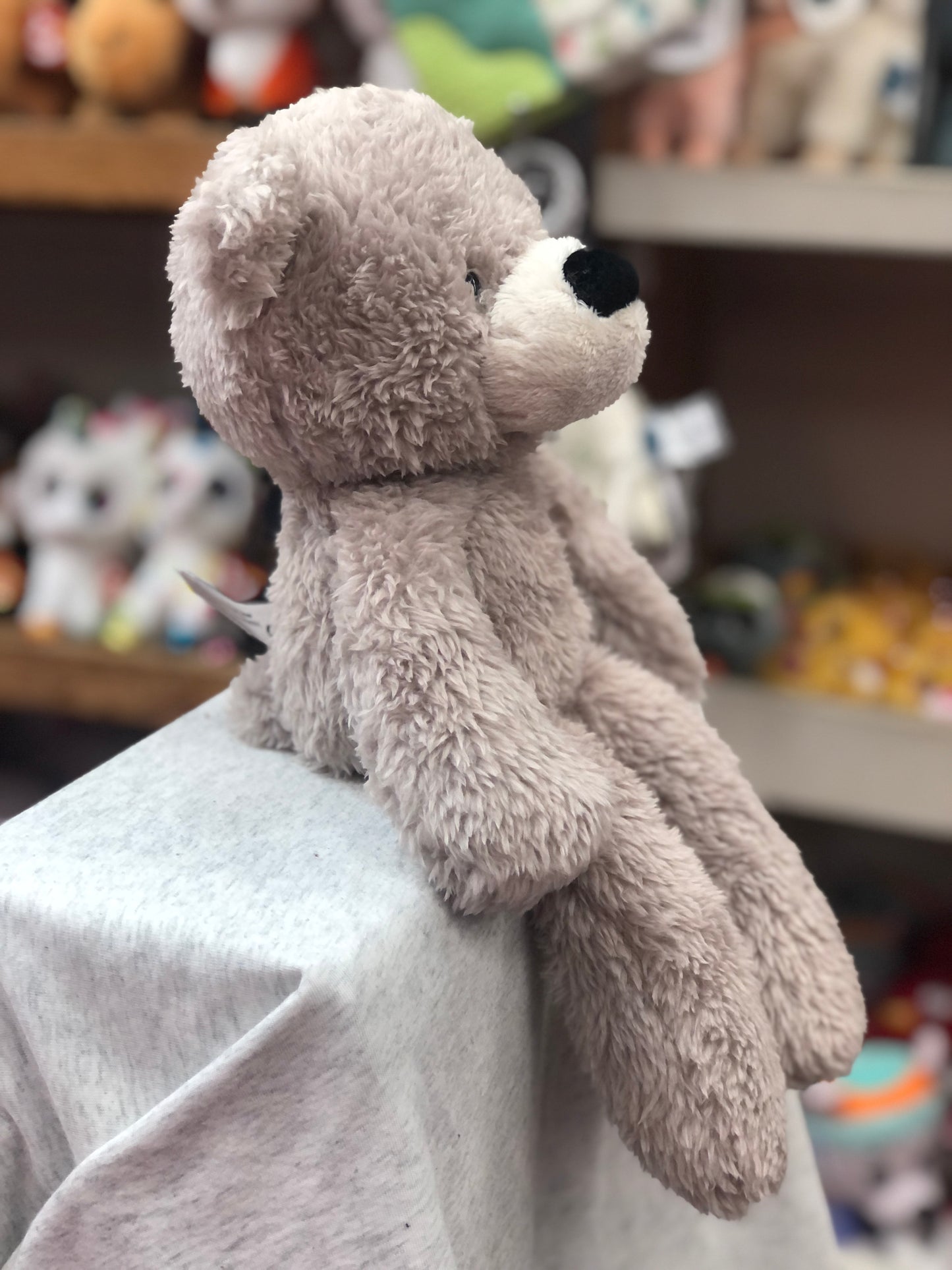 Gund fuzzy gray teddy bear plush toy sitting on display, showcasing its soft texture and cuddly design