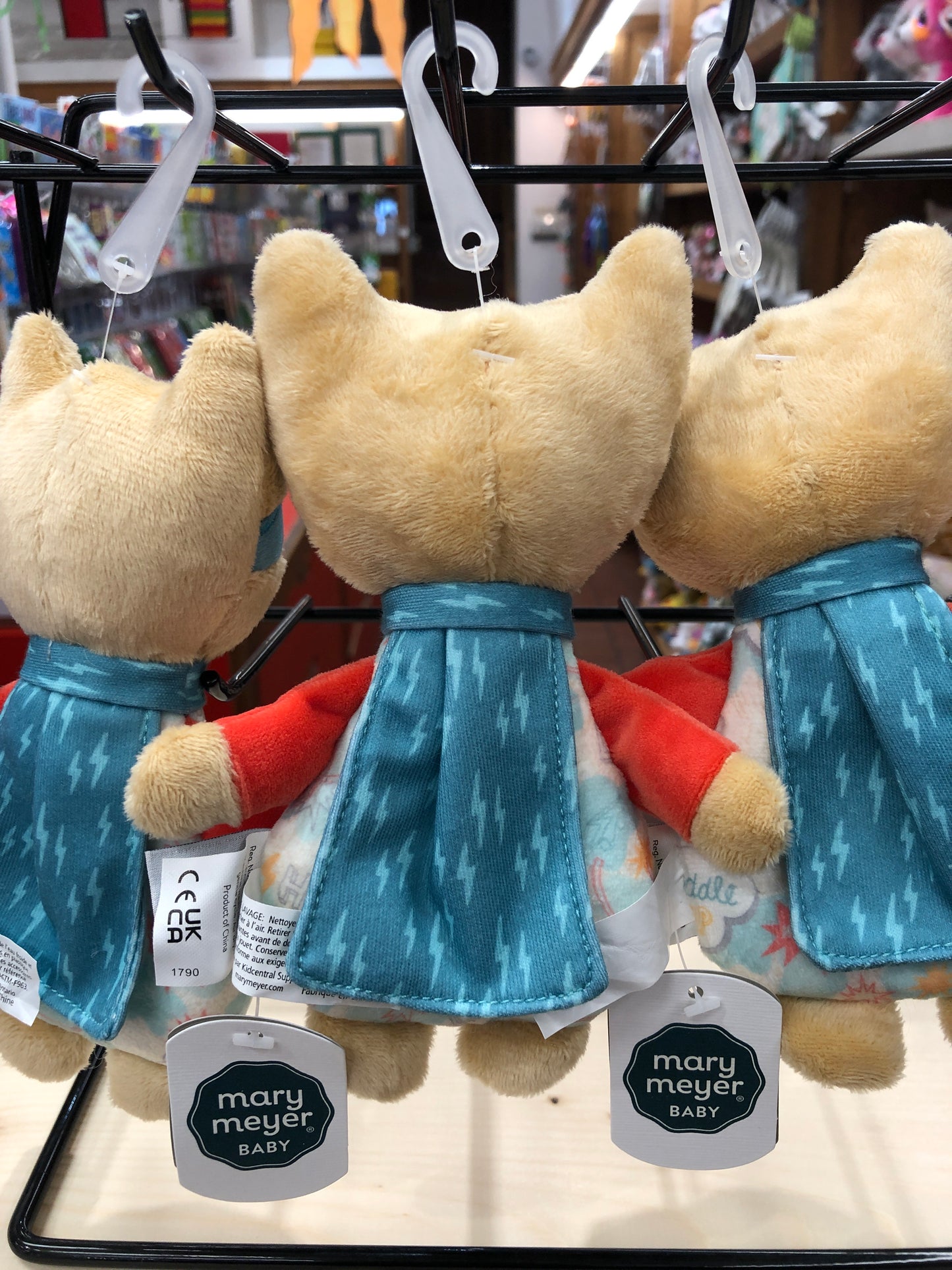 Mary Meyer Lil' Hero baby rattles hanging on display, featuring soft plush bodies with blue capes and red accents, perfect for superhero-themed nurseries