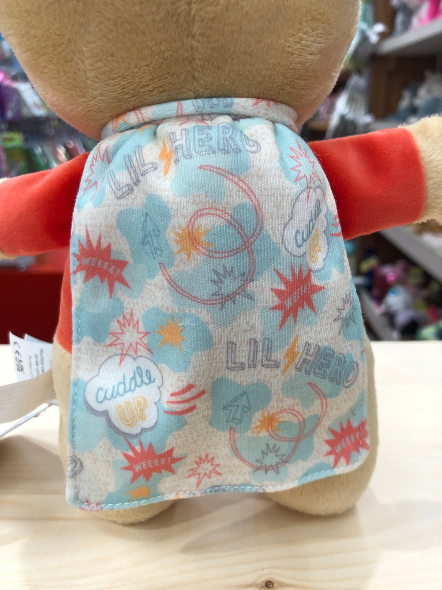 Mary Meyer Lil' Hero plush toy with colorful superhero-themed cape featuring comic book style print and "Cuddle Up" text