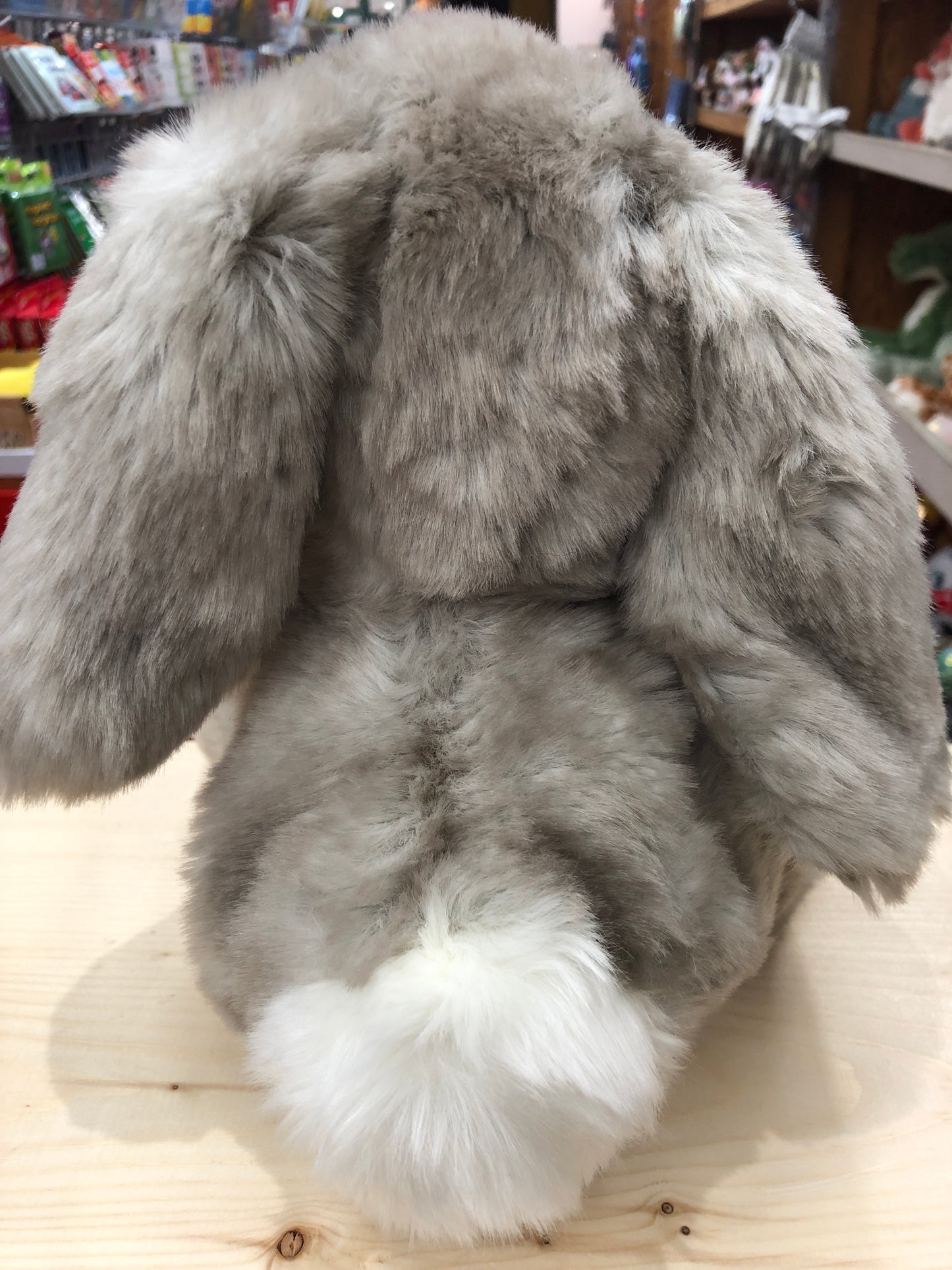 Licorice floppy bunny plush with droopy ears and soft gray fur, sitting on wooden surface in store display
