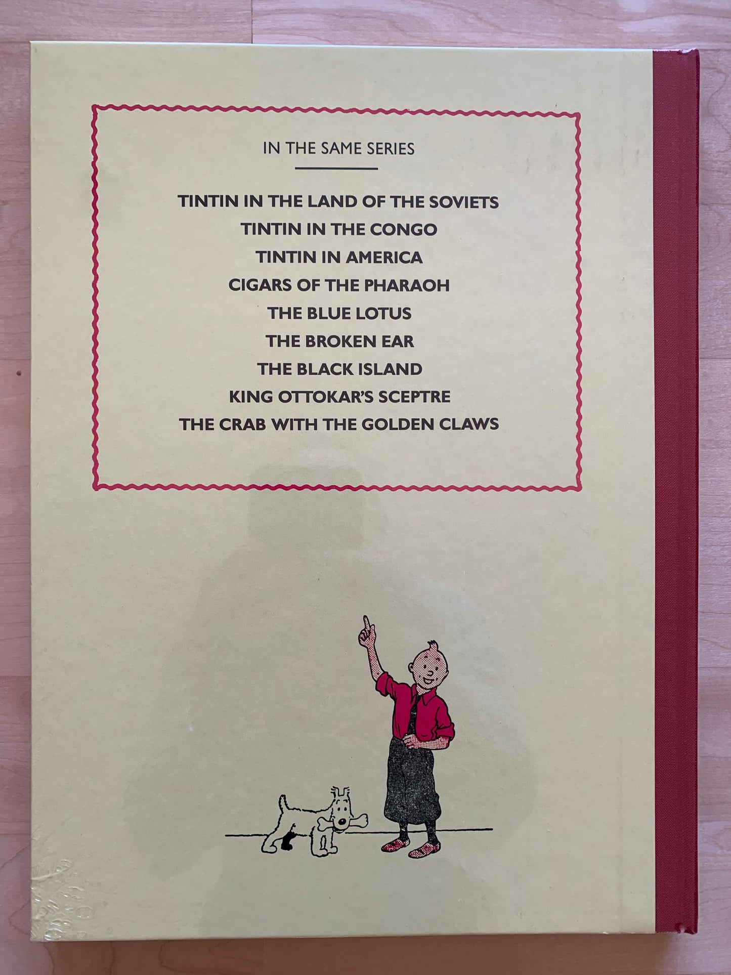Back cover of Tintin book listing other titles in series, with illustration of Tintin and Snowy below. Hardcover in shrink wrap.