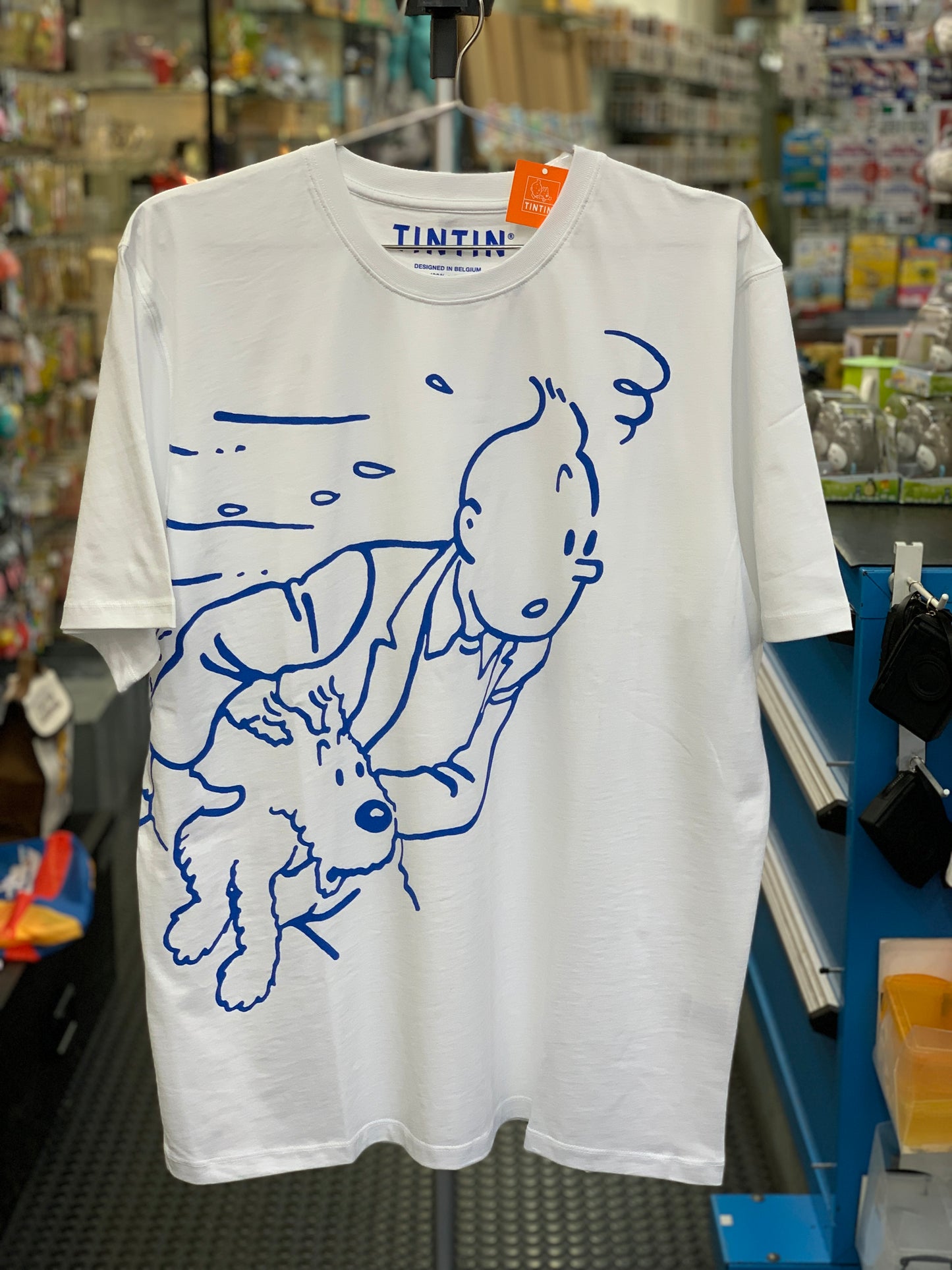 White Tintin t-shirt with blue illustration of Tintin and Snowy running, displayed in store, XL size