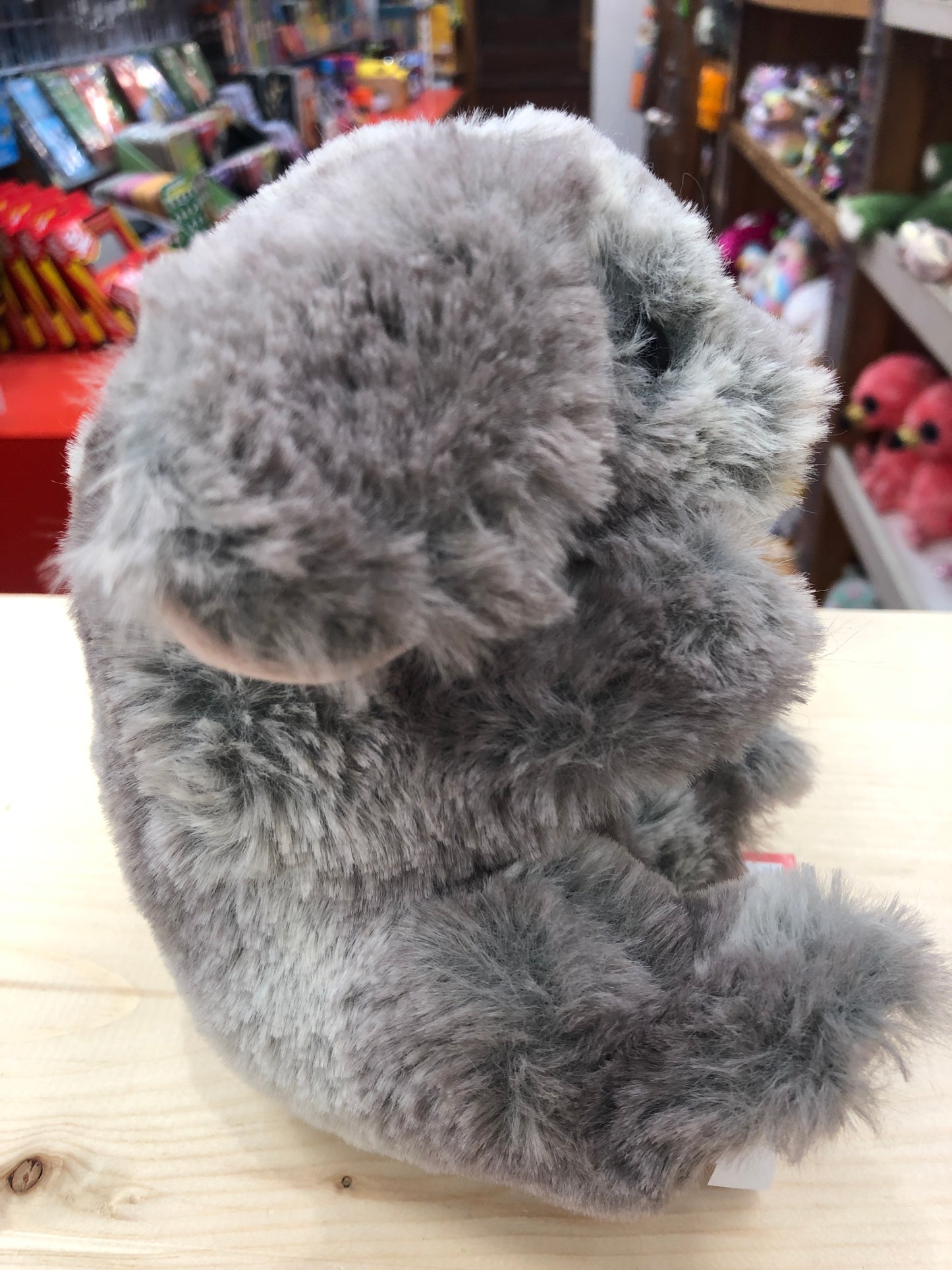 Soft grey Douglas Lil' Handful bunny plush toy on display, lying on its back in a toy store setting