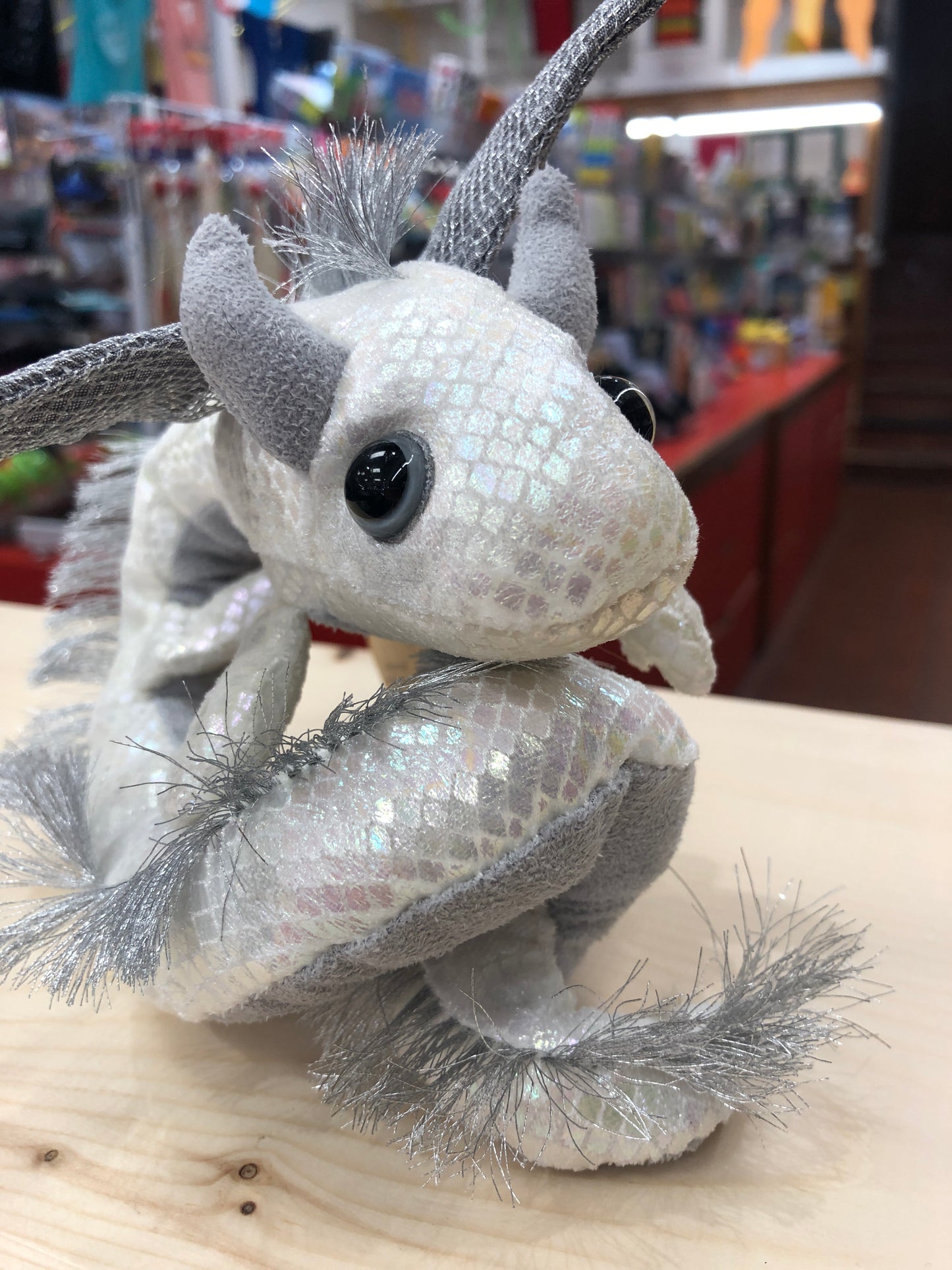 Pearlescent Folkmanis dragon finger puppet with shimmering scales and silver accents, displayed in toy store setting