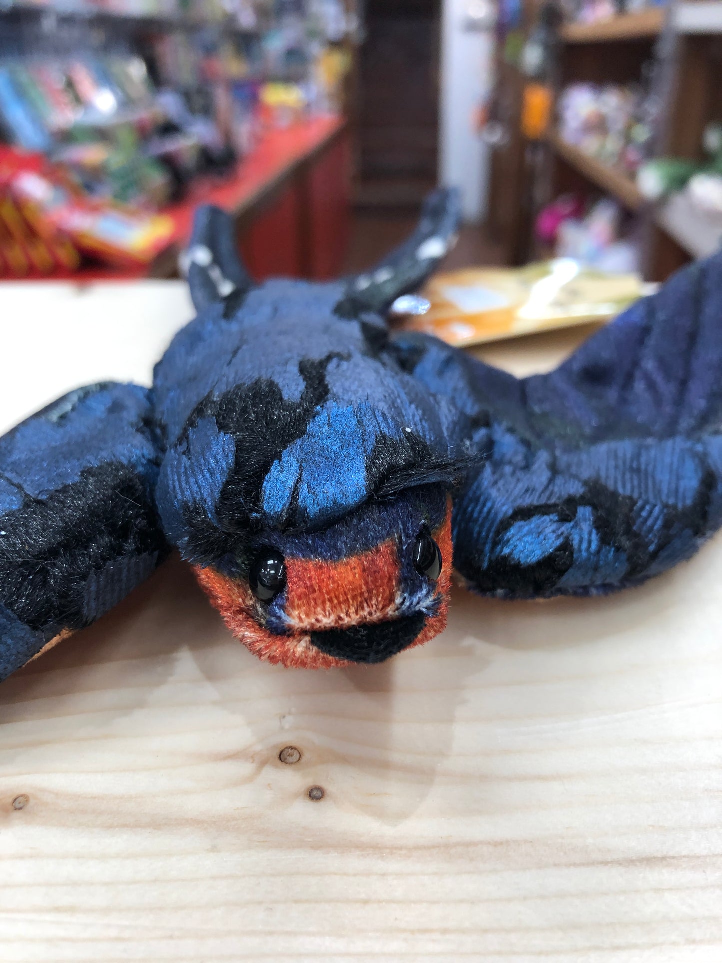 Folkmanis Barn Swallow finger puppet with blue-black plush feathers and orange face, displayed on wooden surface in toy store
