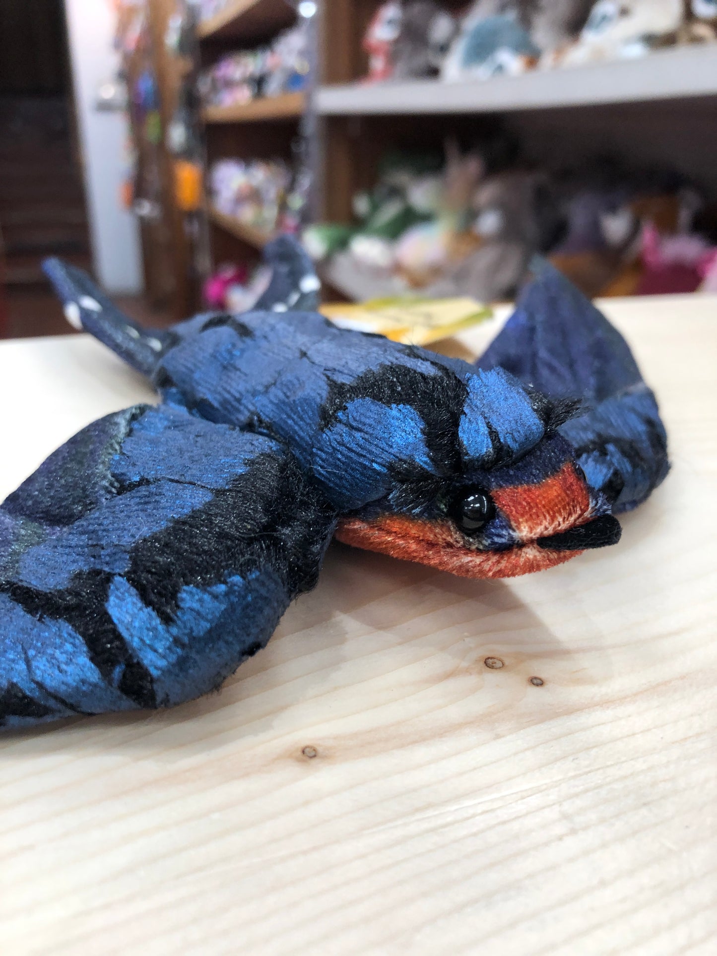 Folkmanis Barn Swallow finger puppet with blue-black plush feathers and cinnamon face, displayed on wooden surface in toy store