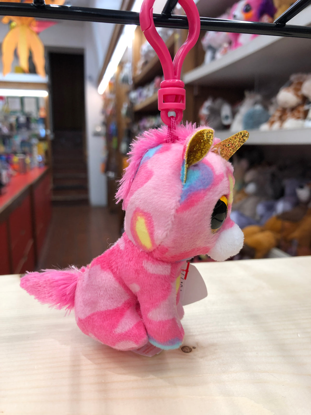 Colorful Ty Beanie Boo Fantasia unicorn plush clip with sparkly eyes and gold horn, displayed in toy store