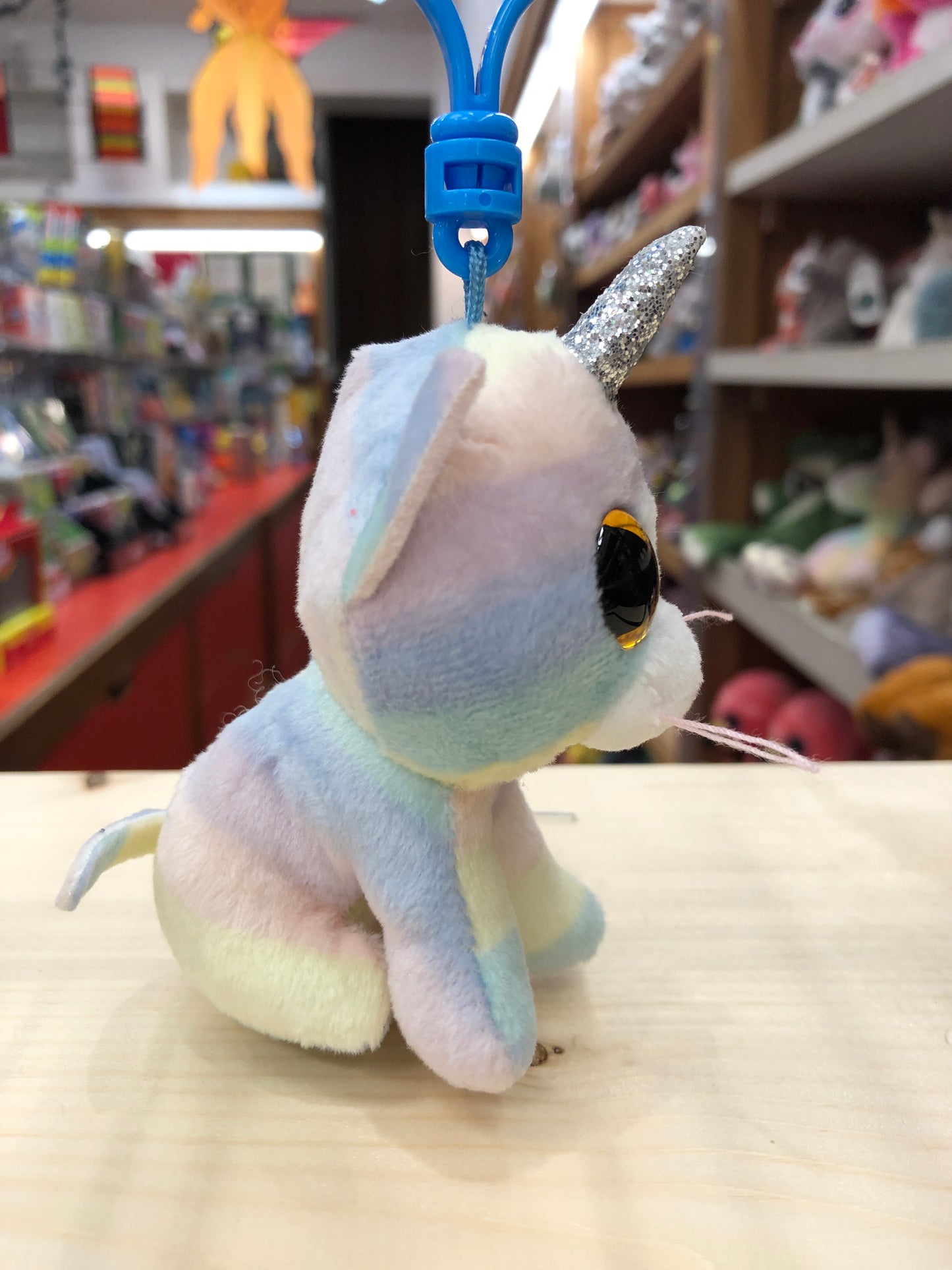 Pastel Ty Beanie Boo unicorn cat plush clip with glittery horn and golden eye, displayed in toy store