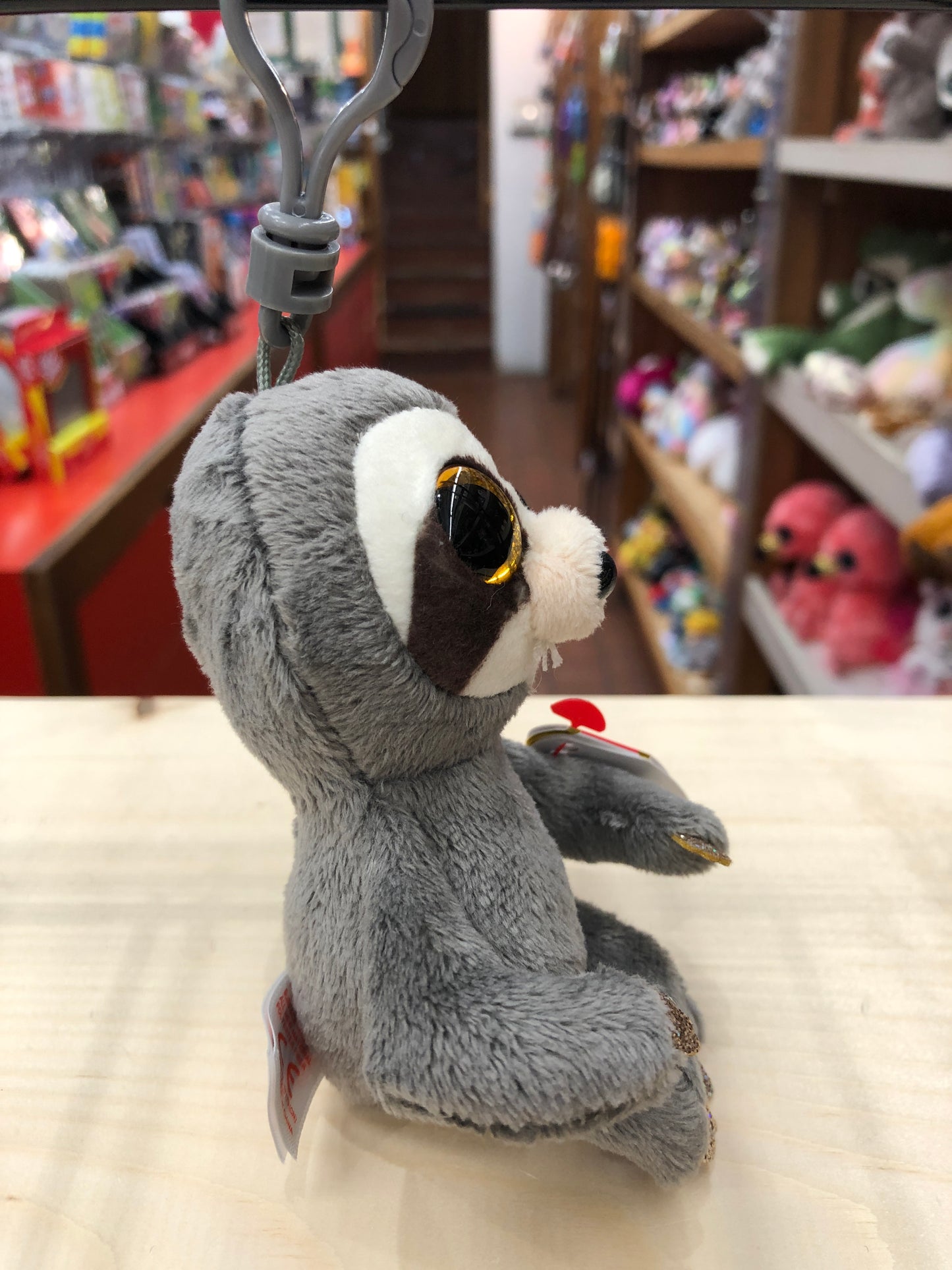 Ty Beanie Boo Dangler sloth plush clip with golden eyes, displayed in toy store, soft gray fur and white face markings