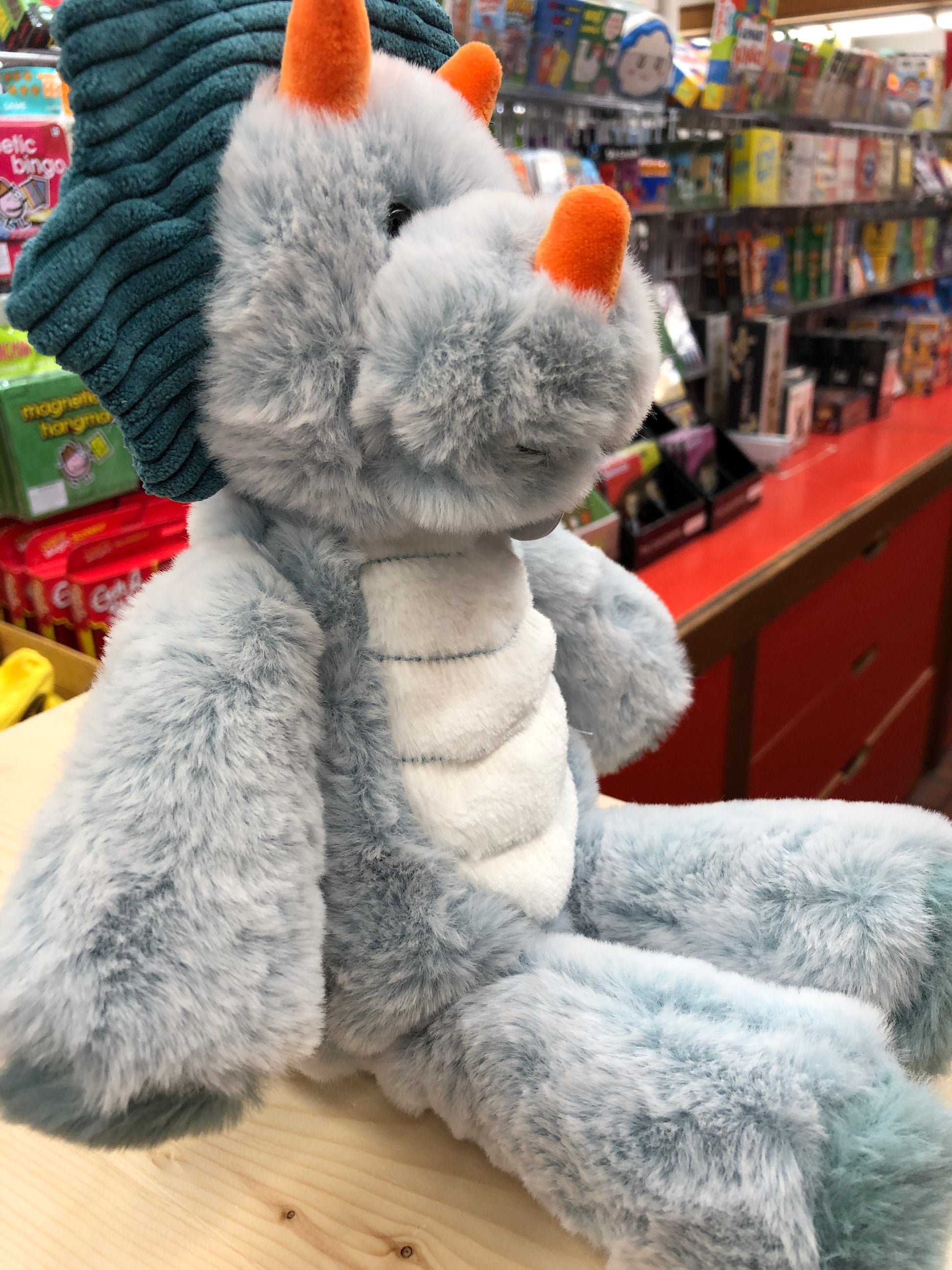 Soft gray Mary Meyer Marshmallow Triceratops plush toy with orange horns, displayed in toy store aisle