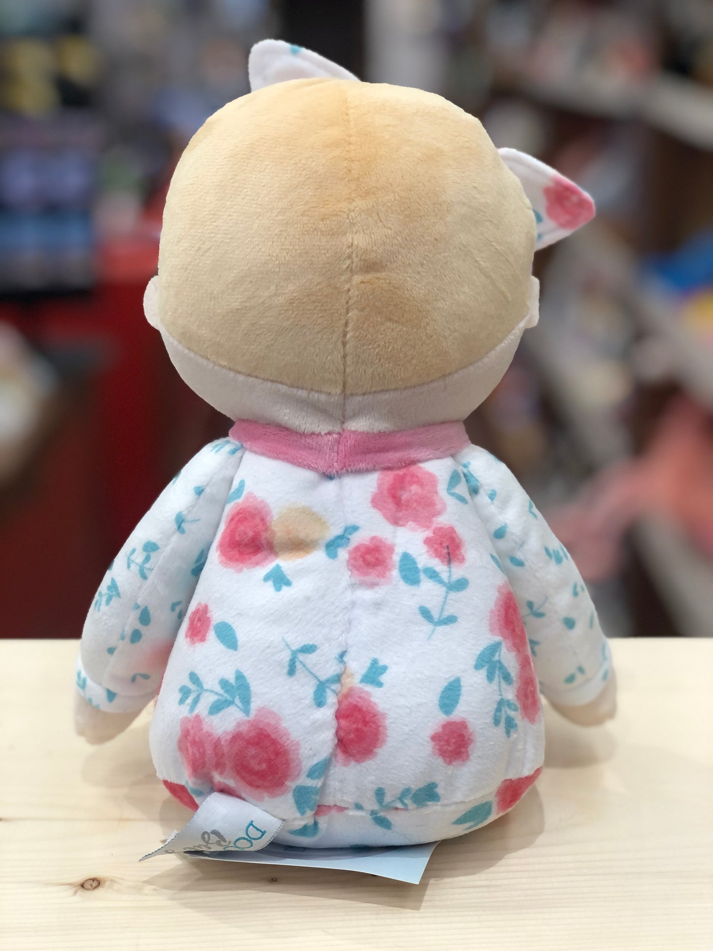 Soft plush baby doll Vera in floral pajamas, viewed from behind, showing pink and blue flower pattern on white fabric
