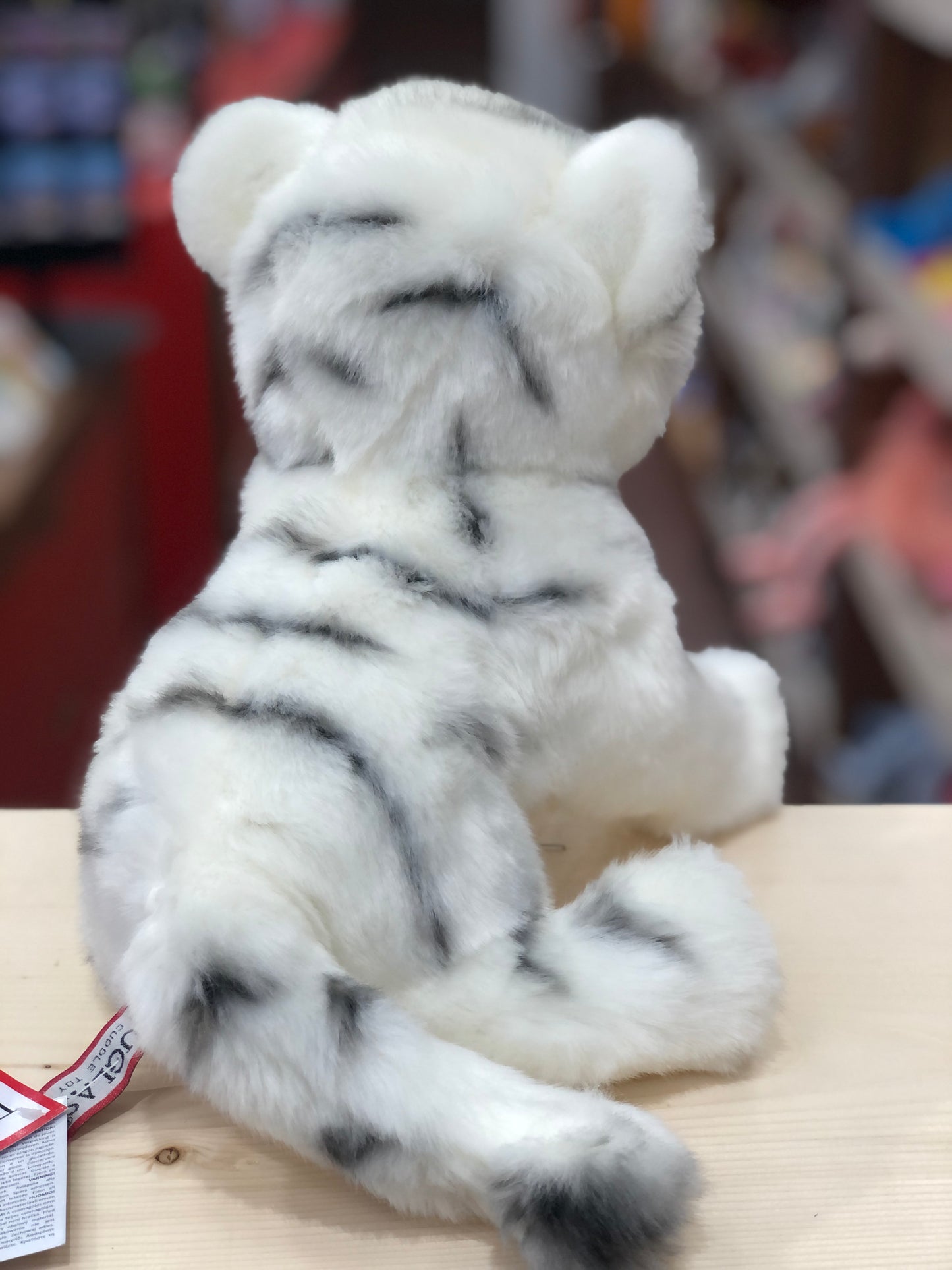 Soft plush white tiger cub toy with realistic striped fur, sitting on wooden surface, viewed from behind
