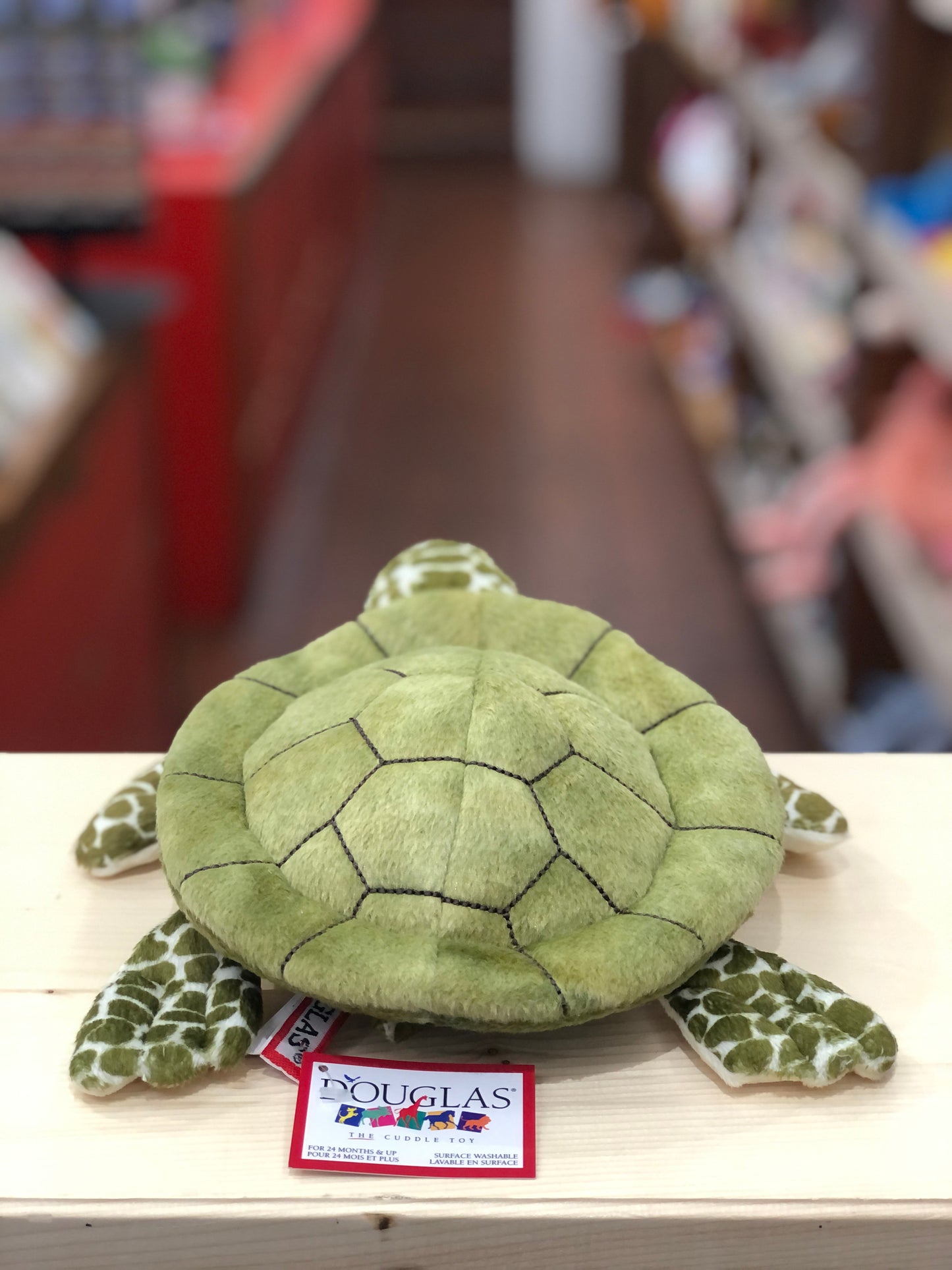 Soft green sea turtle plush toy with realistic shell pattern and floppy flippers, displayed on wooden surface with Douglas tag