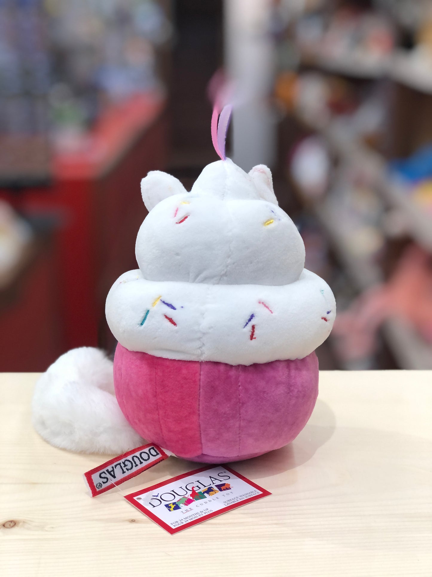 Cute Douglas Cat Cupcake Macaroon plush toy with white frosting, pink base, colorful sprinkles, and fluffy tail on display