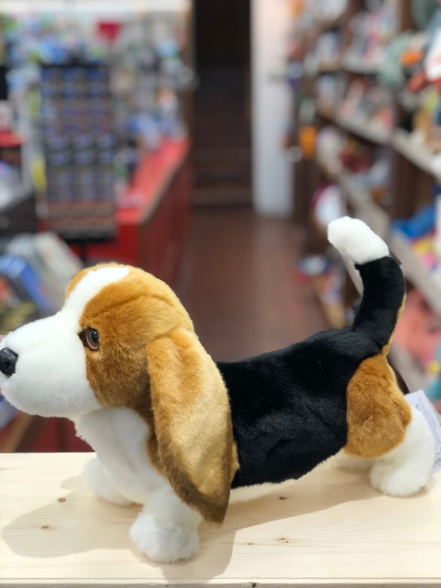 Realistic Douglas Basset Hound plush toy with tri-colored coat, droopy ears, and curved tail in toy store setting