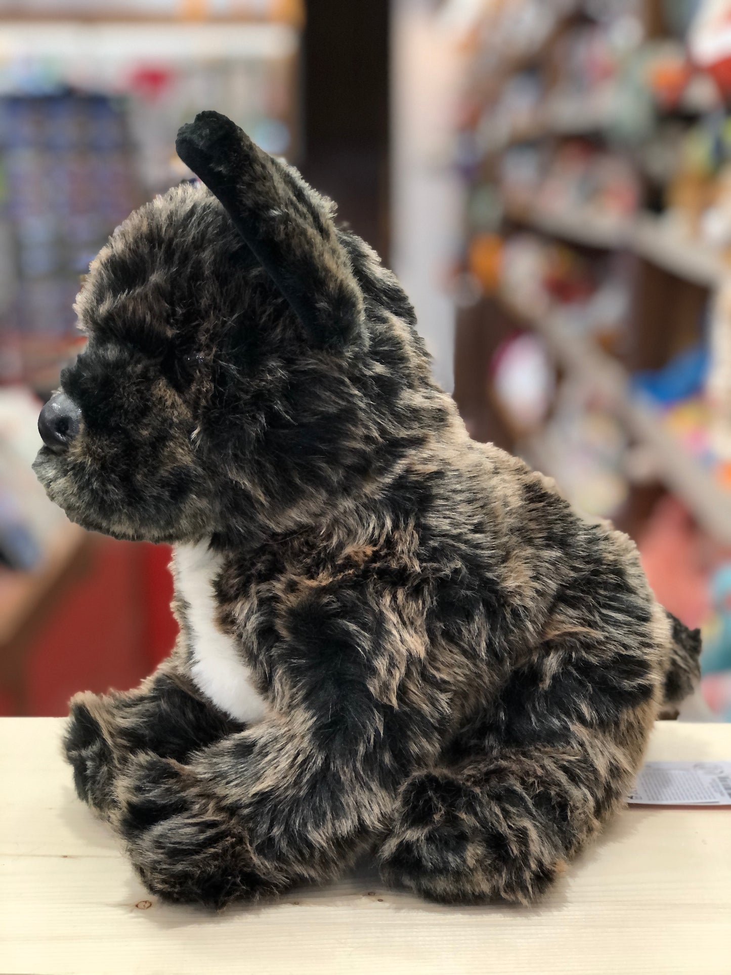 Realistic 12" French Bulldog plush toy with brindle coat, large ears, and amber eyes, sitting on display in toy store