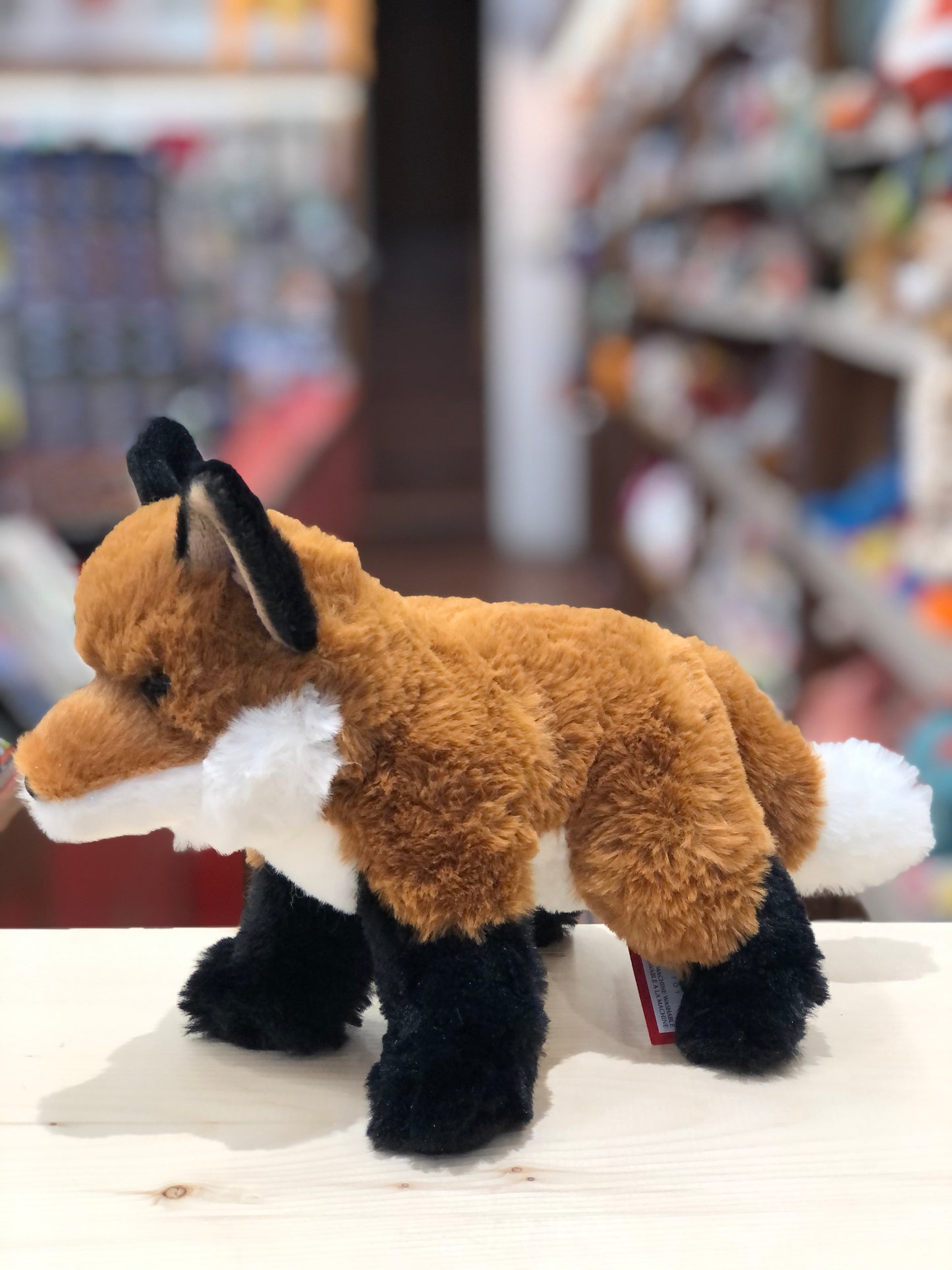 Adorable Mini Freddie Fox plush toy with orange fur, white belly, and black paws, standing on display in a toy store