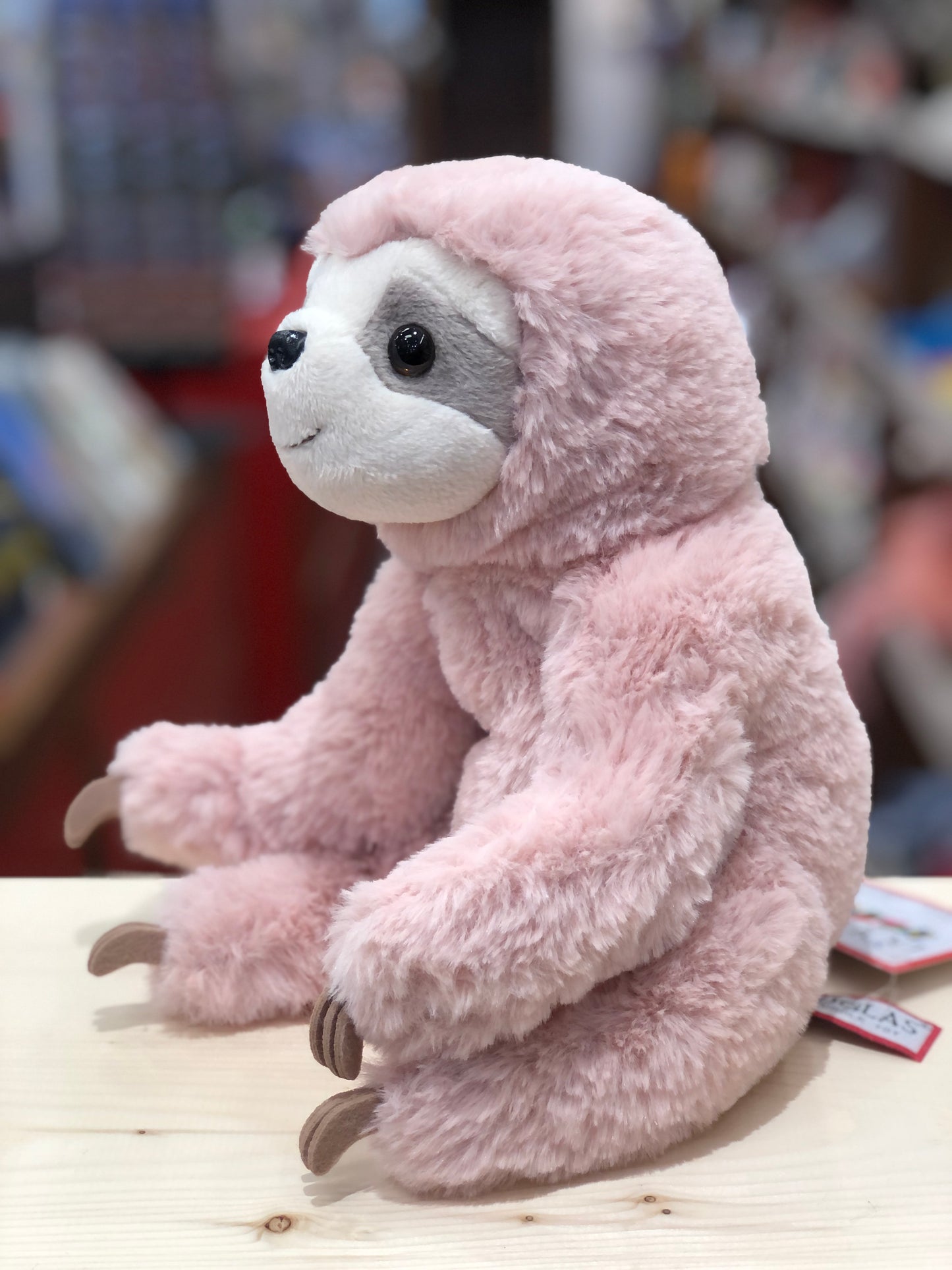Soft pink sloth plush toy with gray face markings, amber eyes, and felt claws, sitting on wooden surface