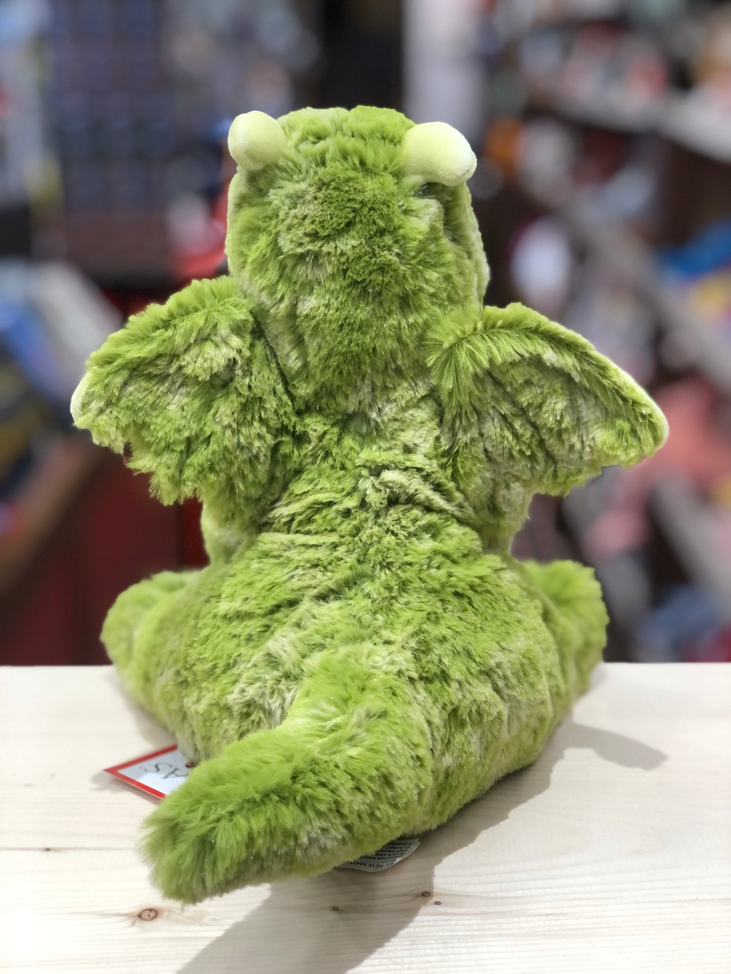 Cuddly green dragon plush toy Lucian with soft fur, wings, and oversized feet sitting on display, showcasing its adorable design