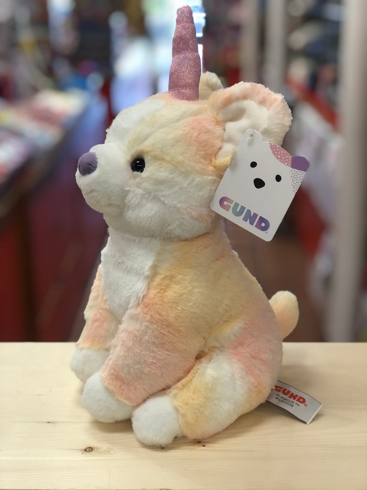 Gund Glamour Corgicorn plush toy with pastel orange fur, pink sparkly horn, and GUND tag, sitting on wooden surface